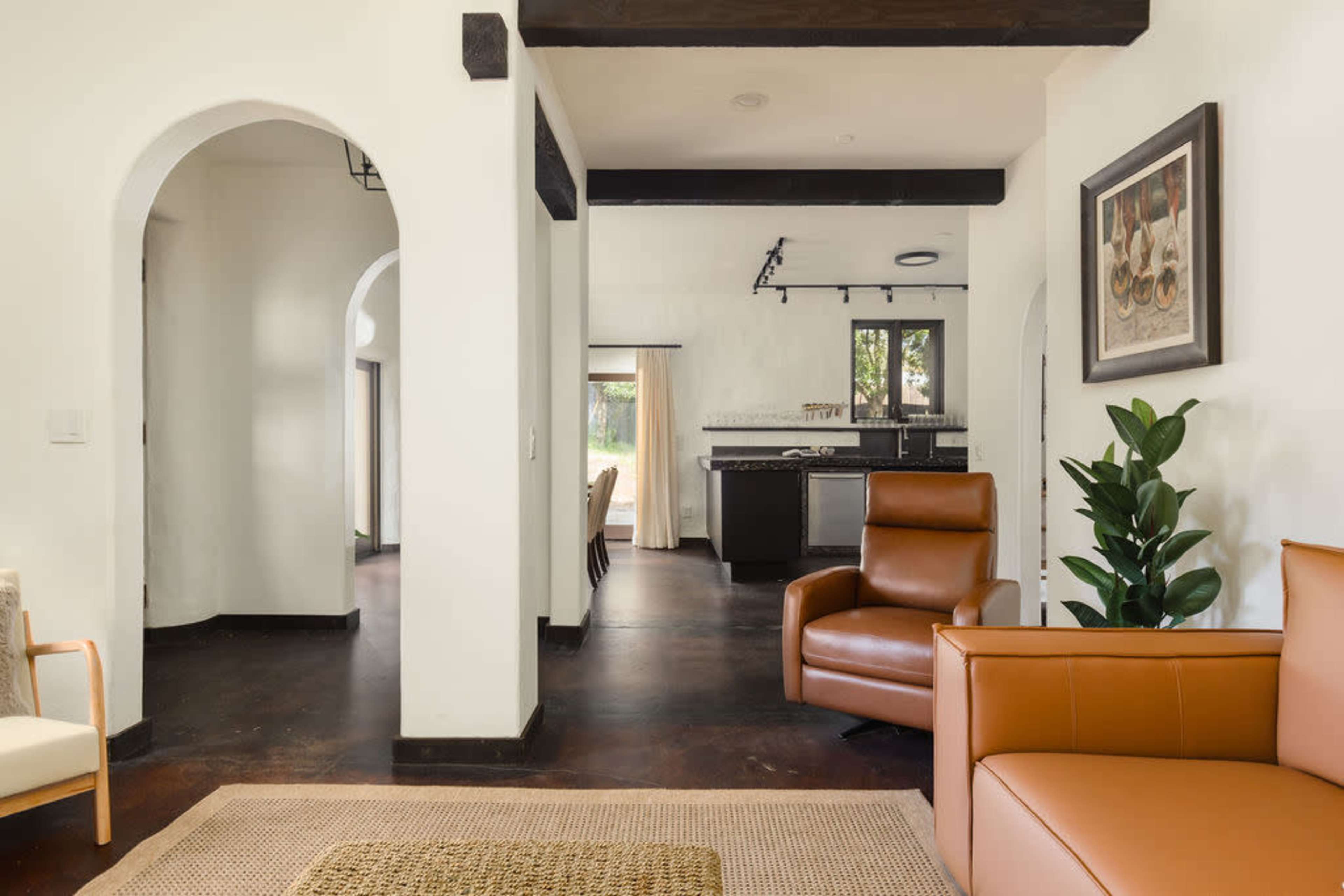 A modern interior space with an open layout, featuring a living area with a brown leather chair, a rug, and a view into a kitchen area.