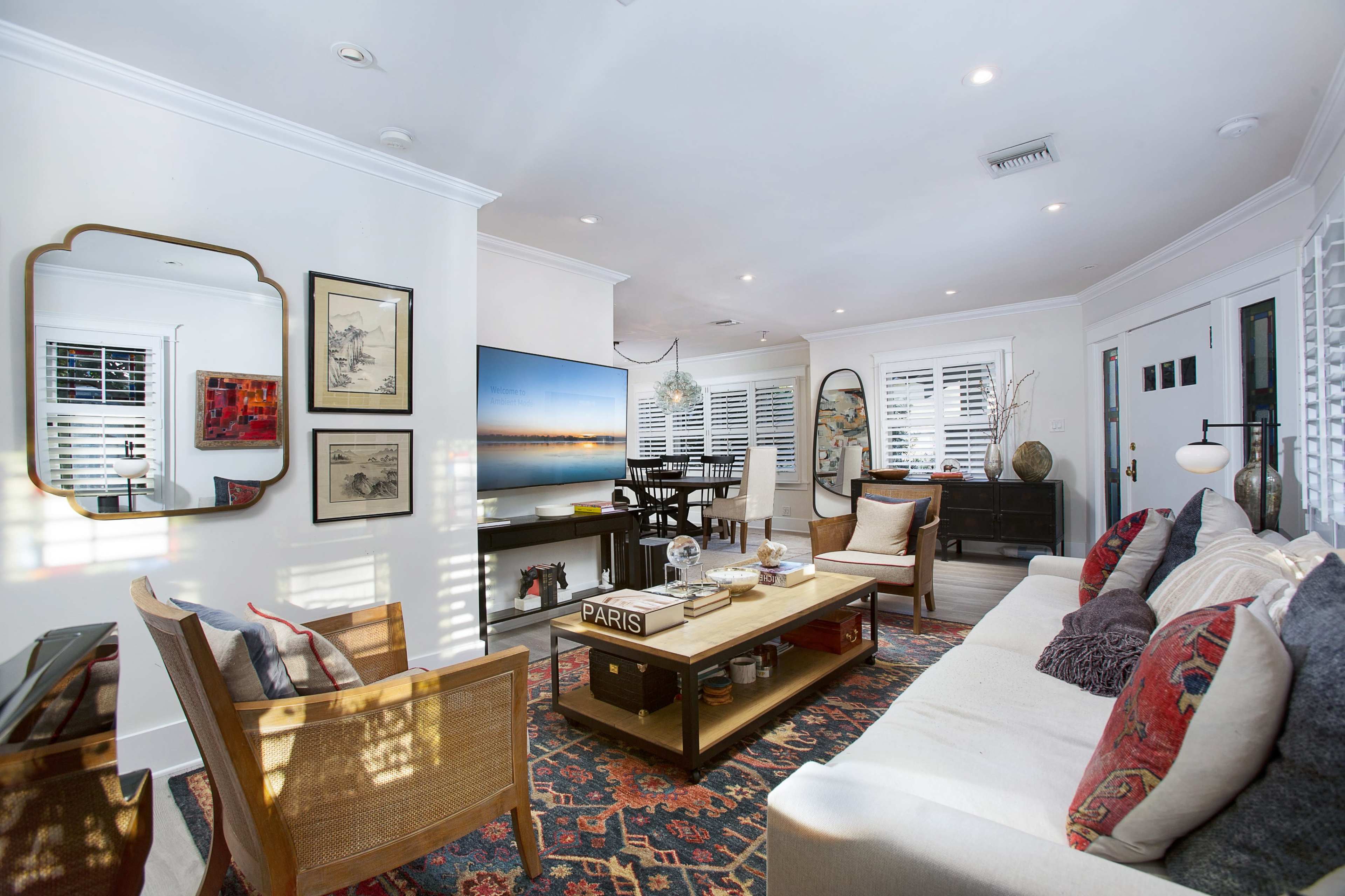 A modern living room with a beige sofa, a wooden coffee table, a large television, and framed artwork on the walls.