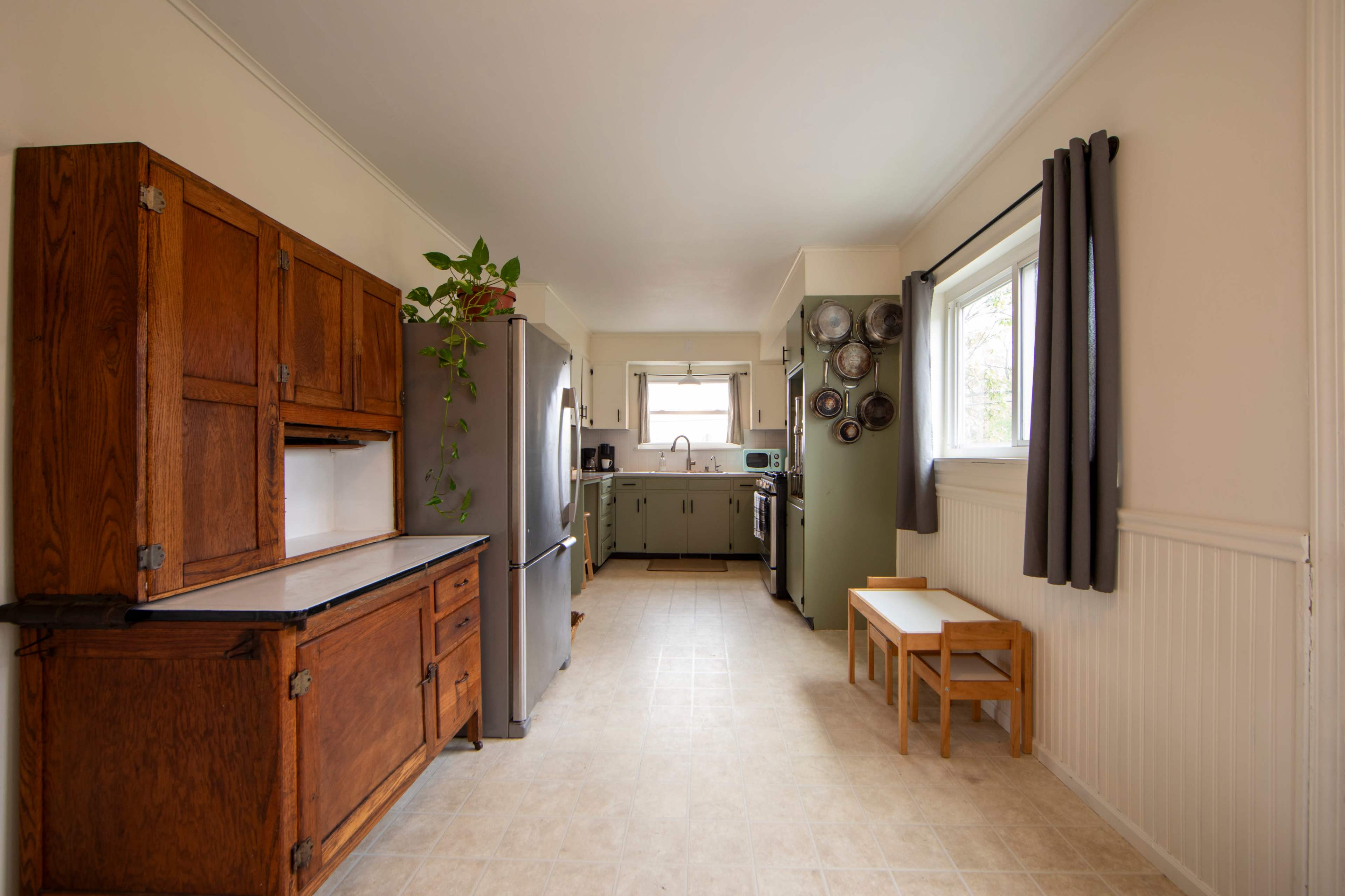 The image shows a modern kitchen with wooden cabinetry, a refrigerator, and a bench near a window.
