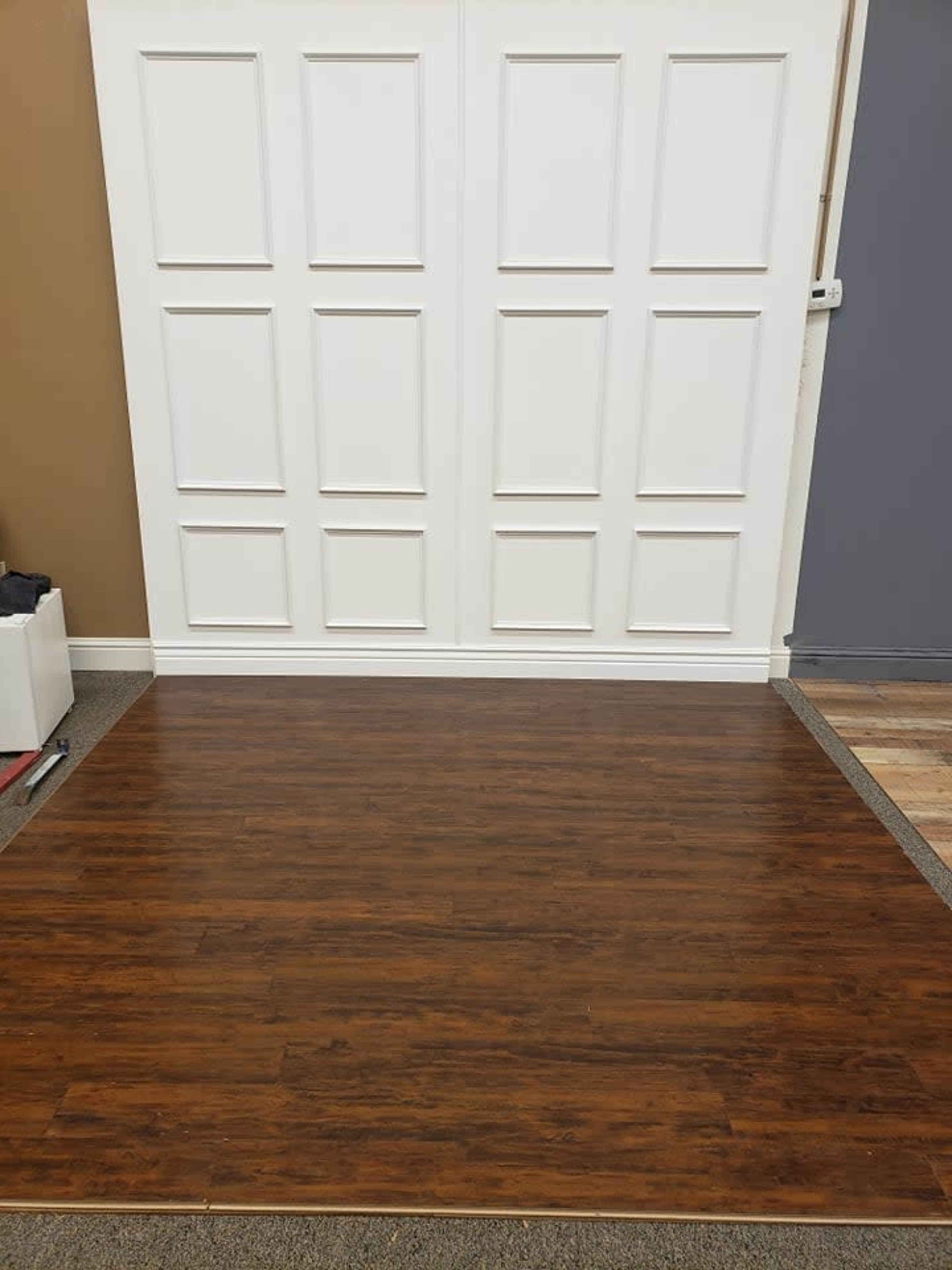 A room with a dark wooden floor and a white paneled wall, complemented by grey walls on one side.