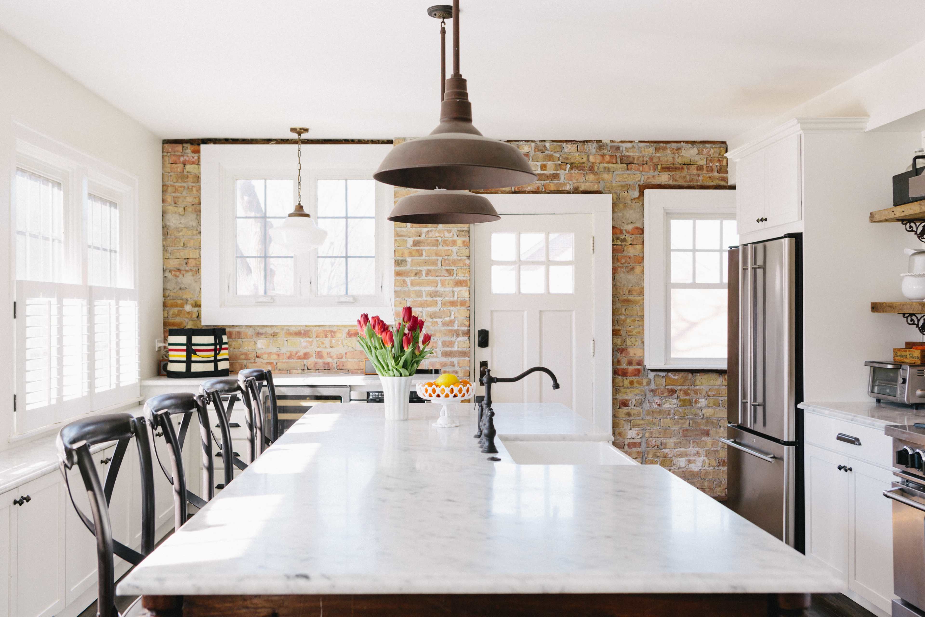 The kitchen features a marble island, stainless steel appliances, and exposed brick walls with a row of barstools.
