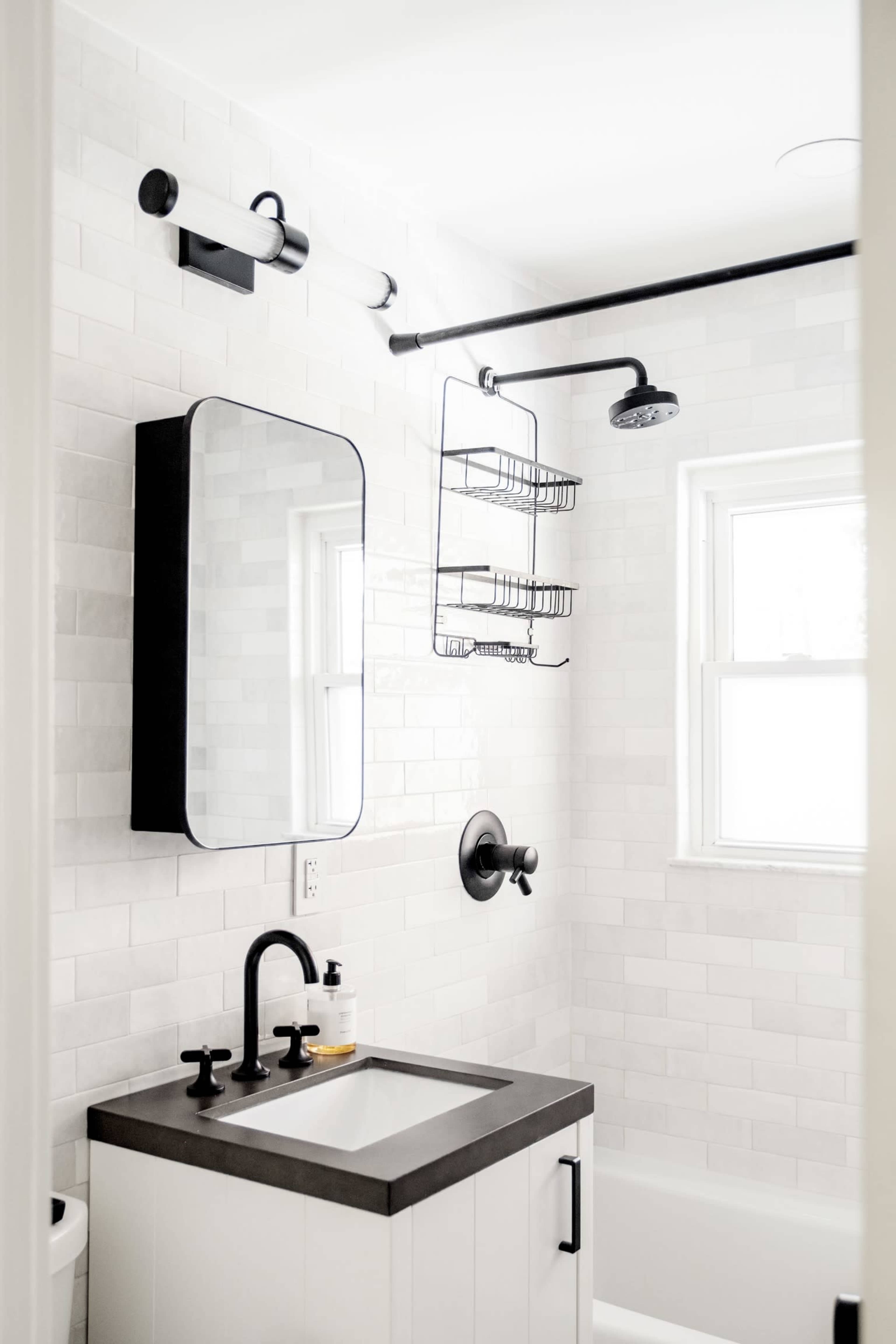 A compact bathroom features a wall-mounted mirror, a black shower head, and a wire rack for storage.