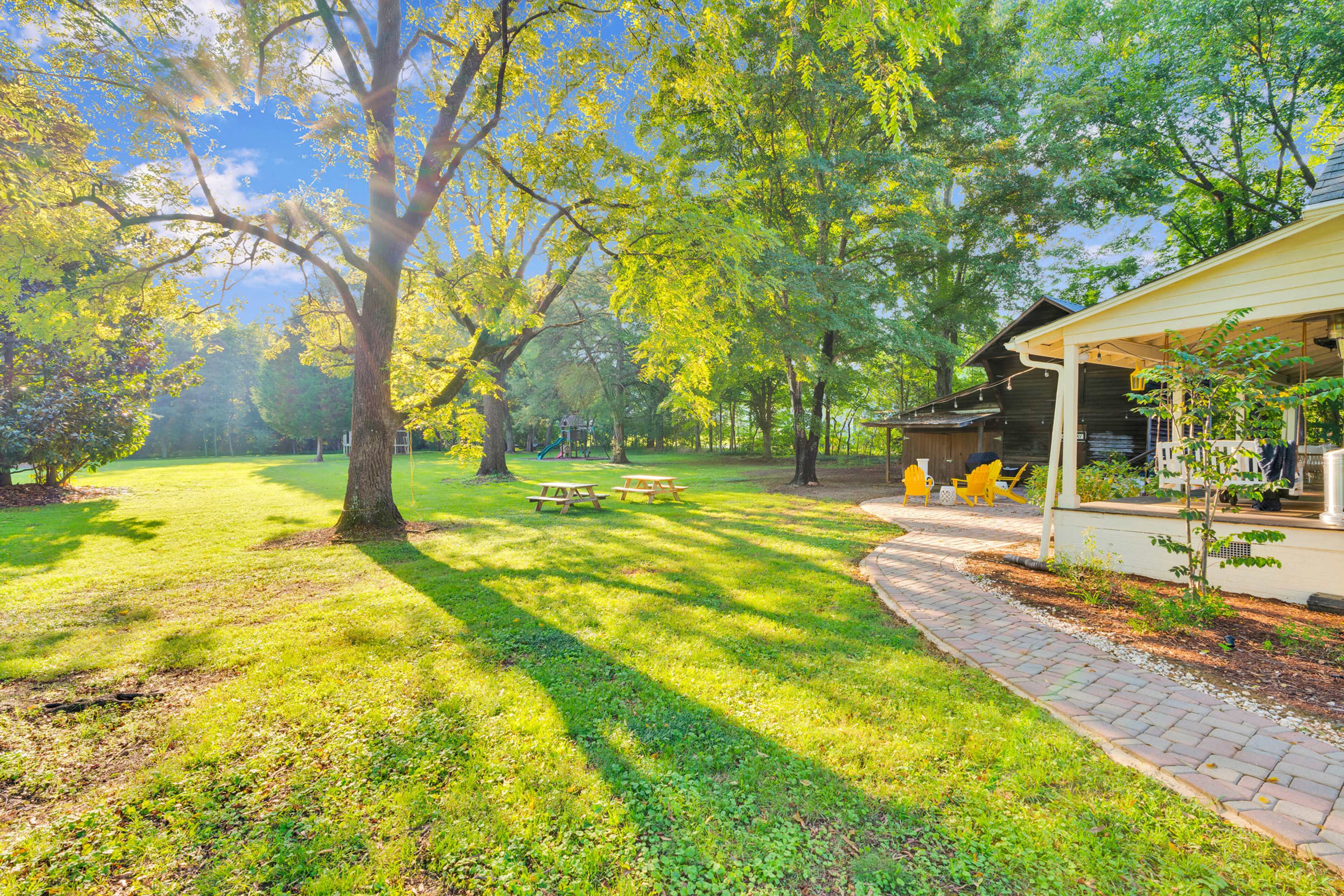 The image shows a grassy outdoor area with trees, a picnic table, and a porch leading to a house.