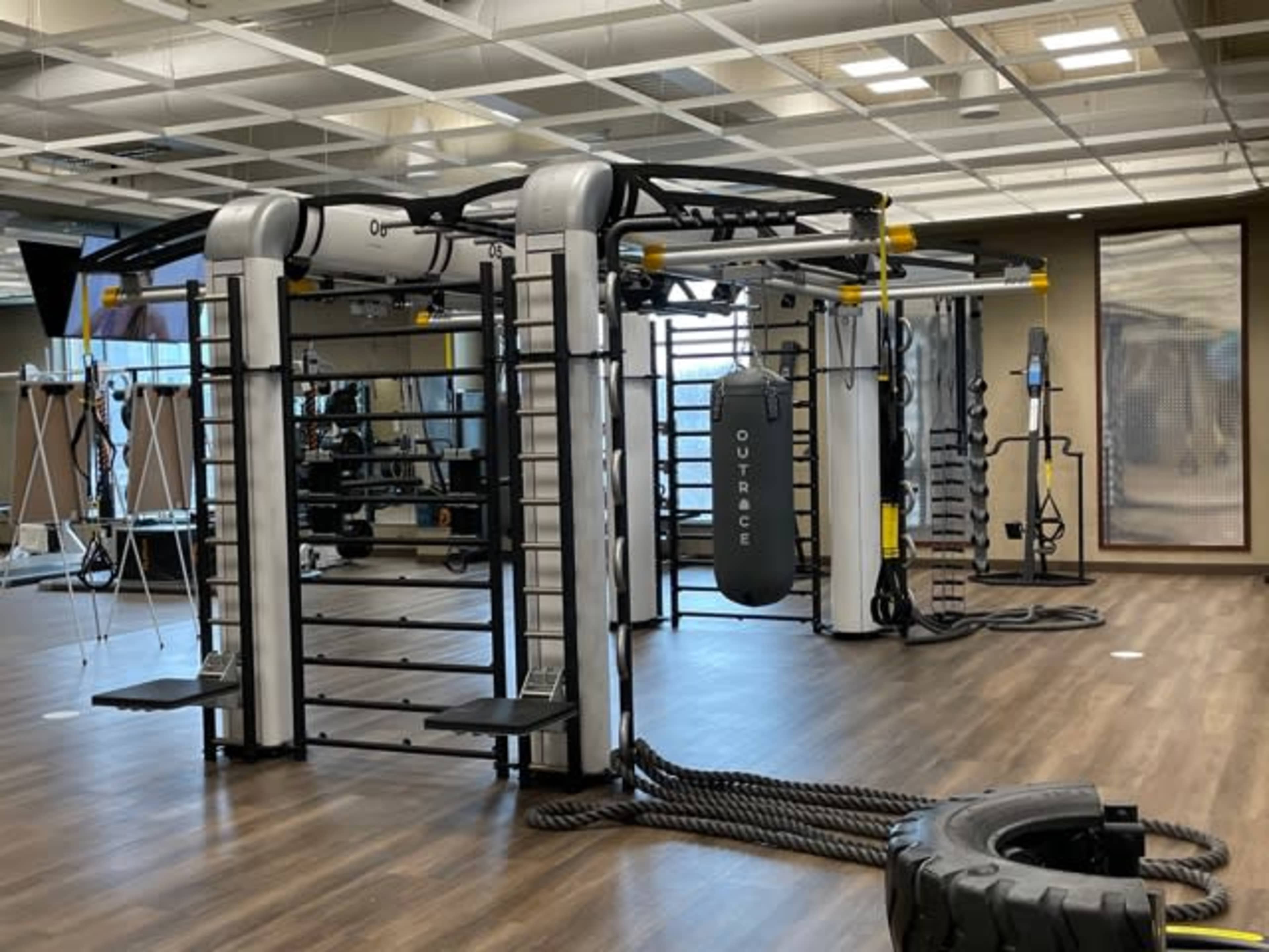 A modern gym facility features a multi-functional training apparatus with ropes and a punching bag in a spacious, well-lit room.