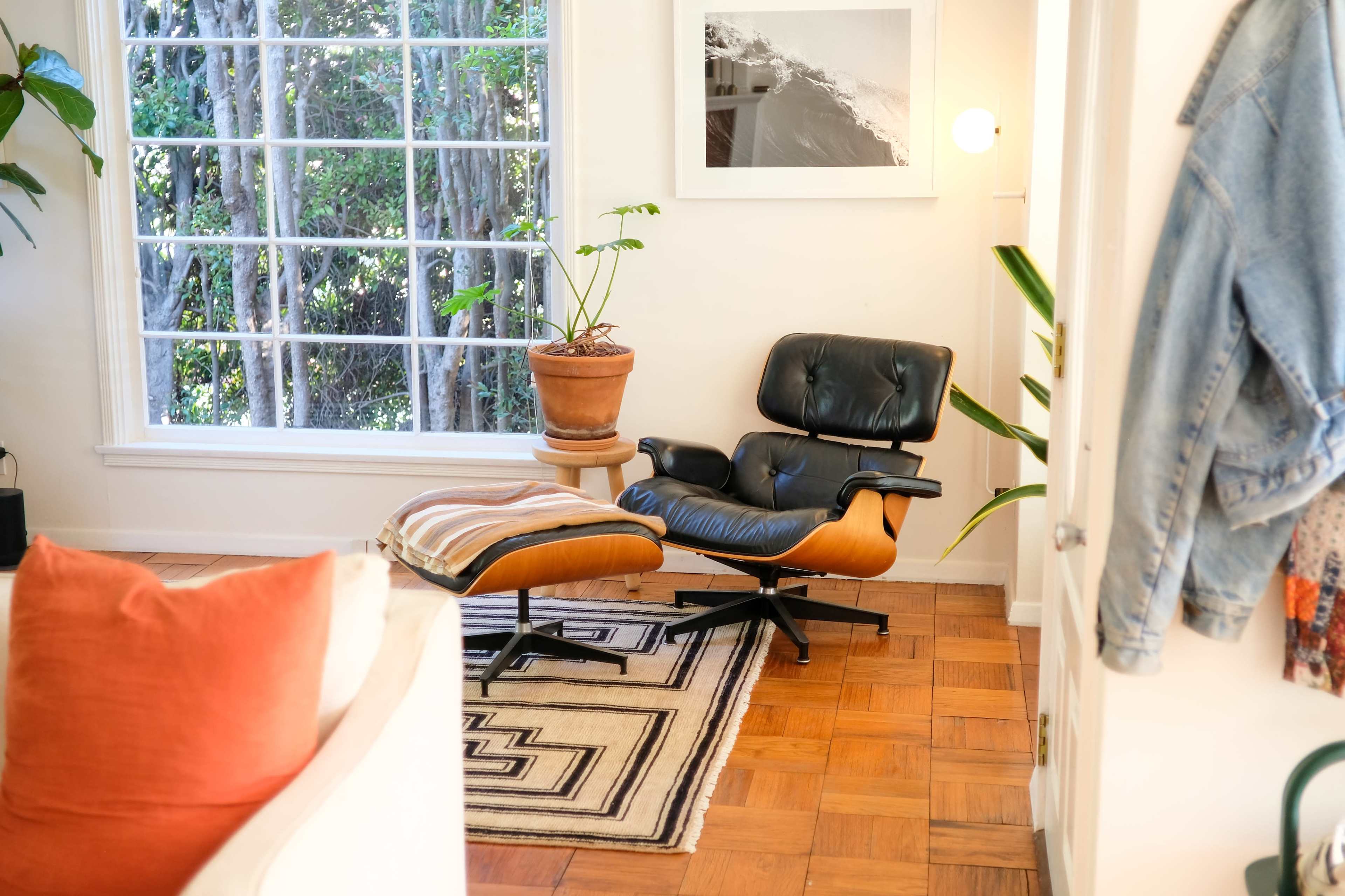 A black ergonomic chair with an accompanying ottoman sits beside a window with greenery visible outside.