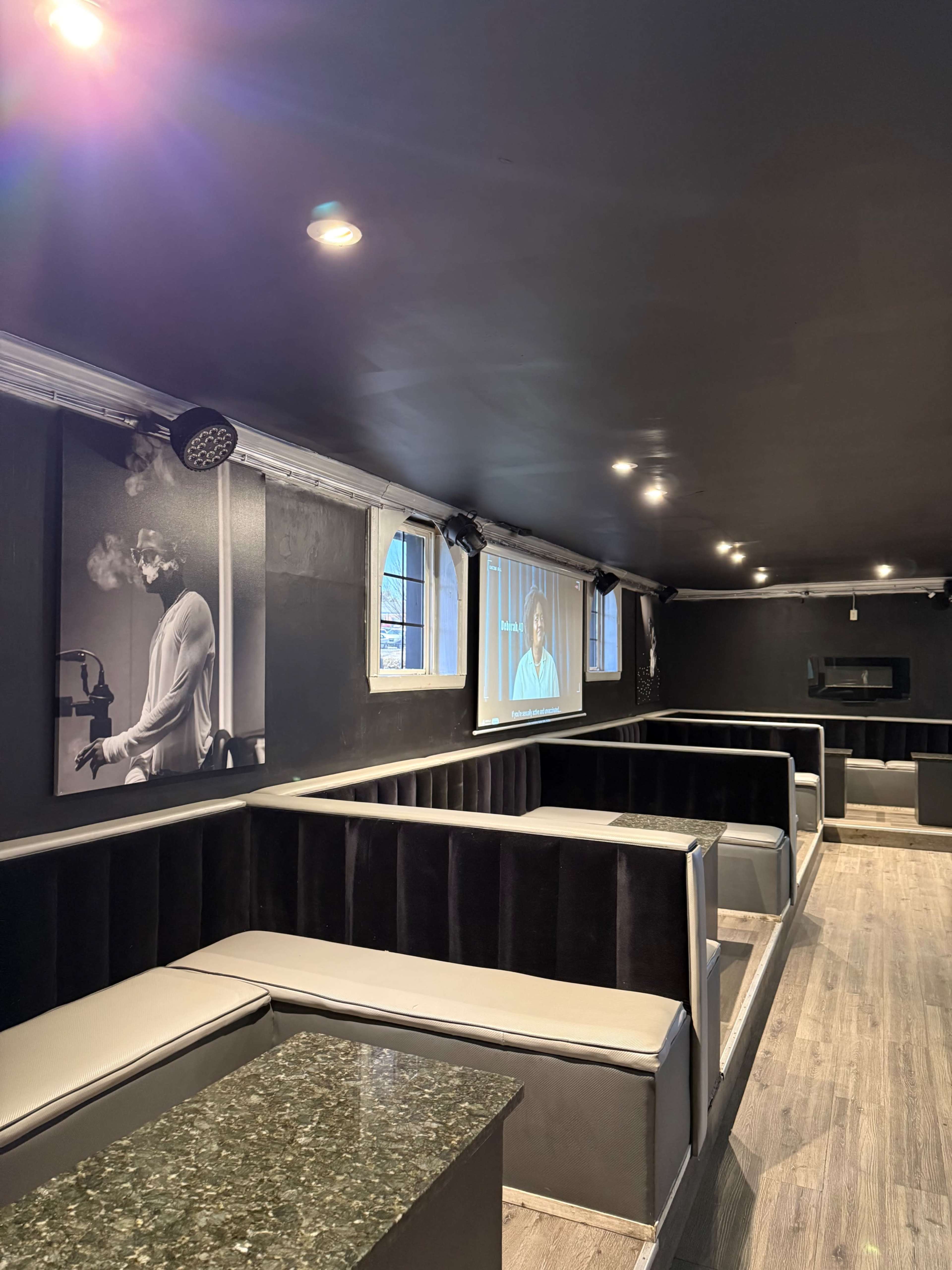 The image shows a modern, dimly lit lounge with cozy seating areas and large windows, featuring artistic black-and-white photographs on the walls.