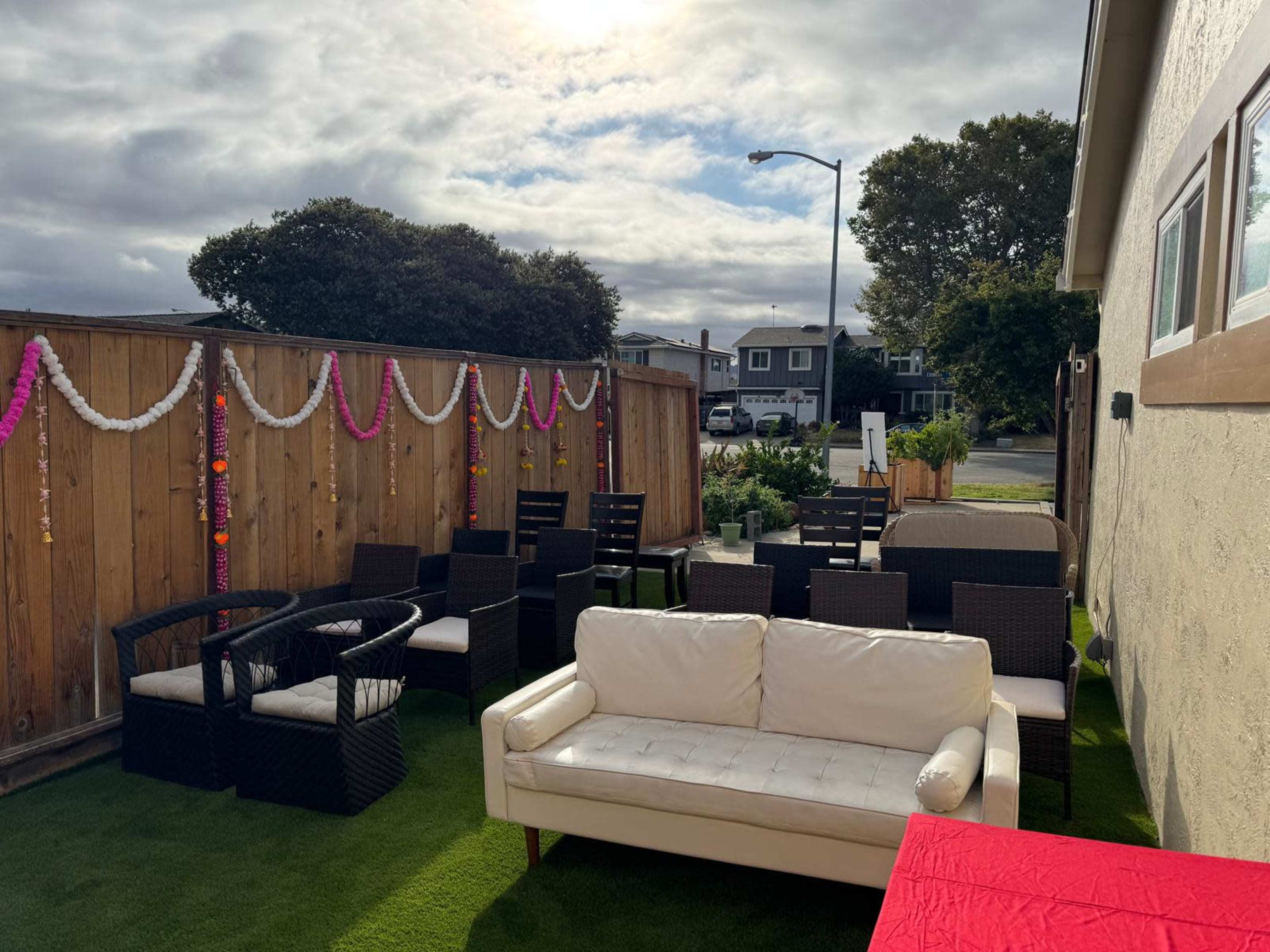 A patio area with black wicker furniture and a white couch, decorated with hanging garlands, under a cloudy sky.