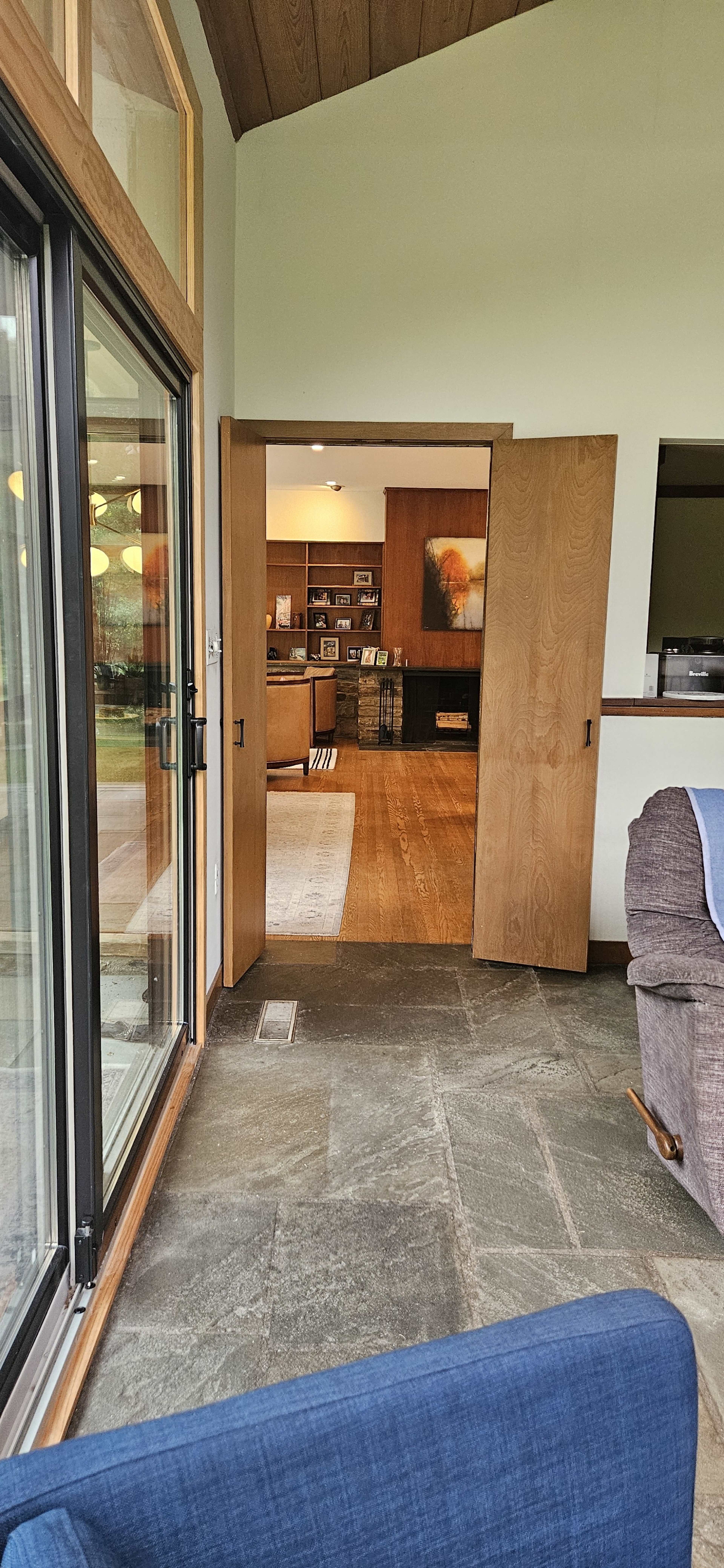 The image shows an interior view of a home, featuring an open doorway leading to a room with a wooden floor and a large window that opens to the outdoors.