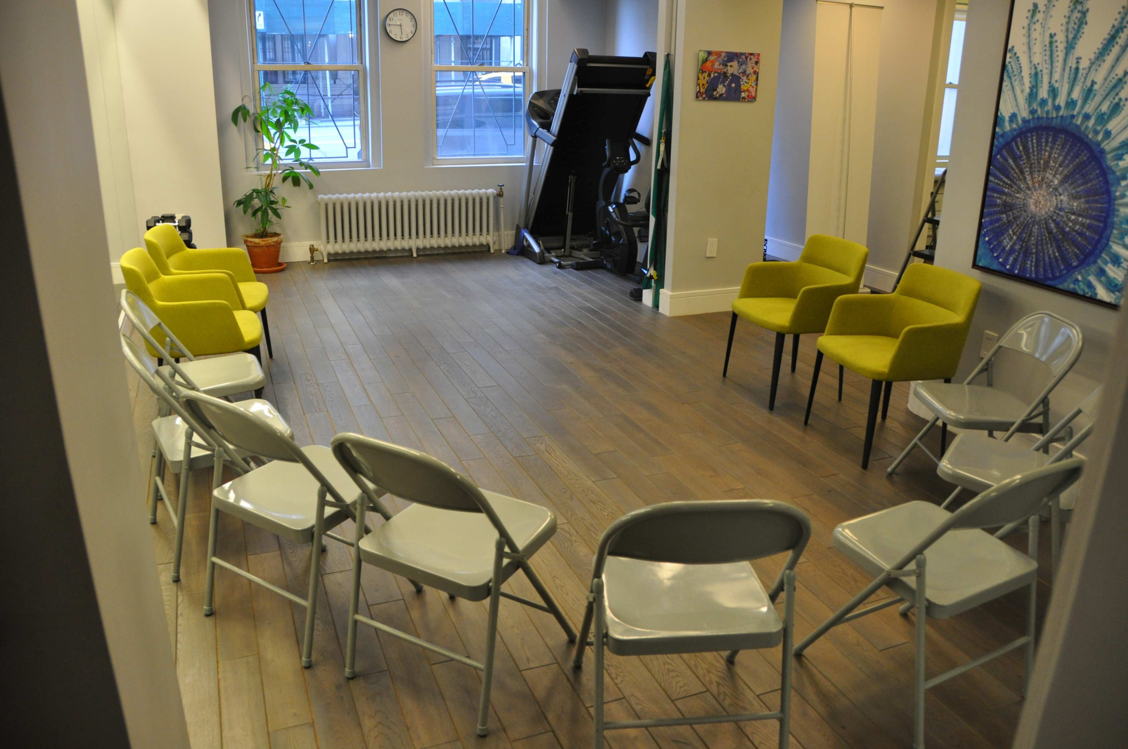 A room with a circular arrangement of folding chairs, a large exercise machine, and a clock on the wall.