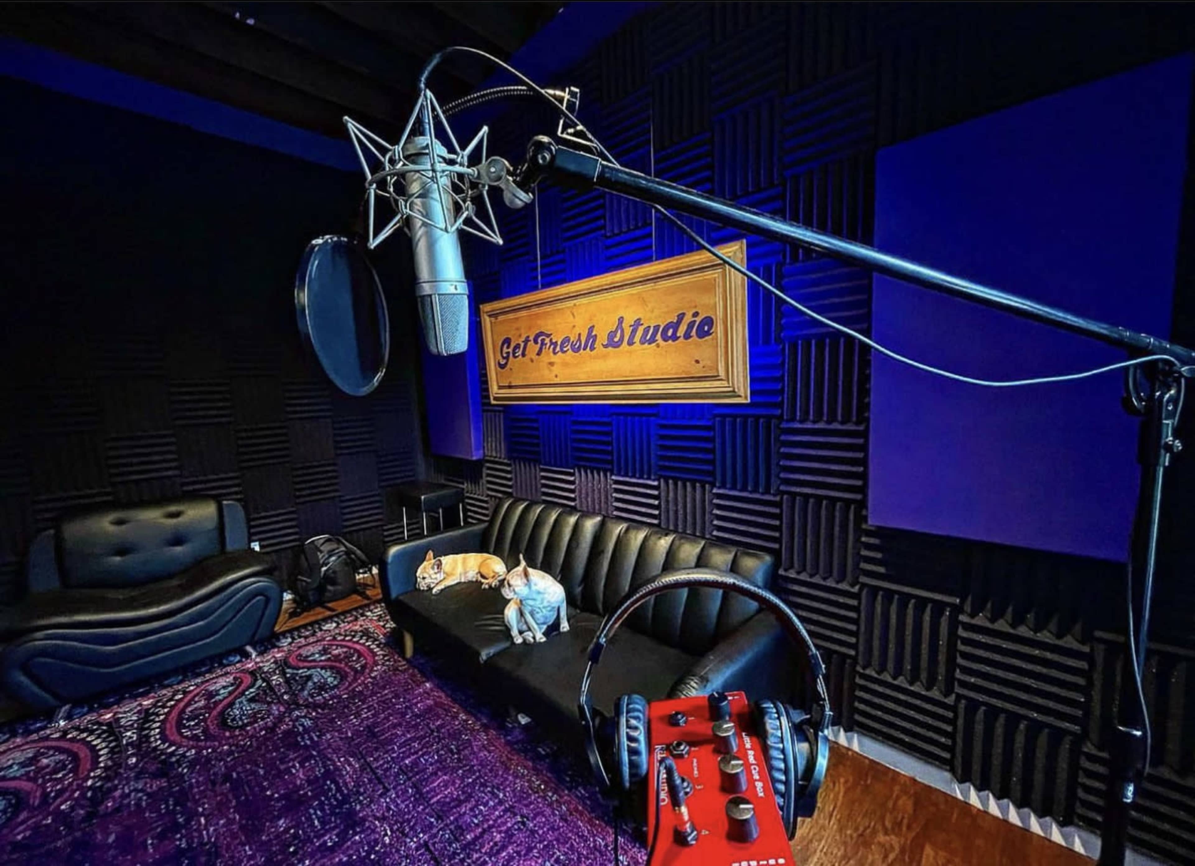 A recording studio featuring a microphone on a stand, a black sofa, and a red audio interface on the floor.