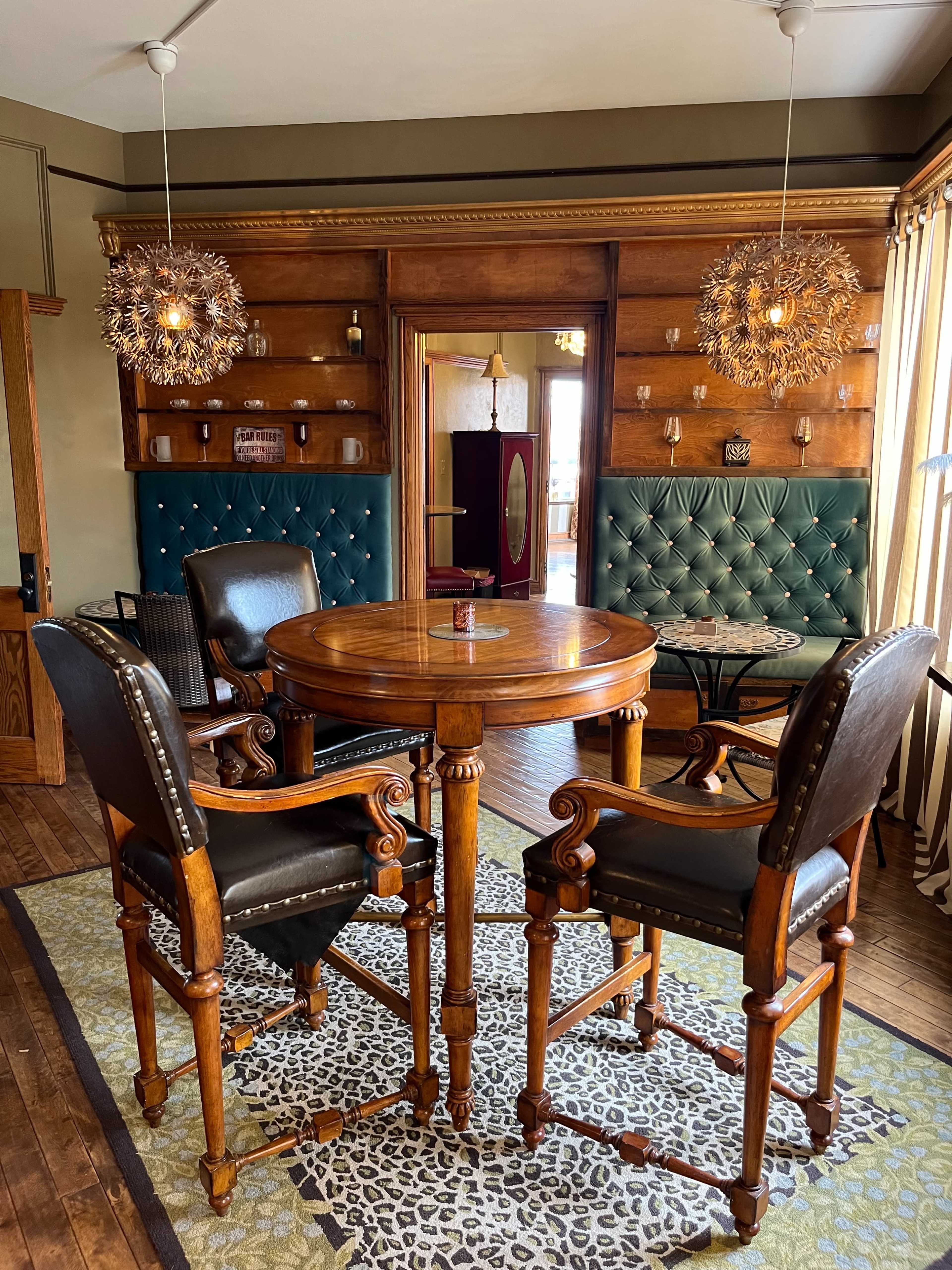 A restaurant interior featuring a round wooden table surrounded by two black leather chairs and a green upholstered wall with decorative lighting.