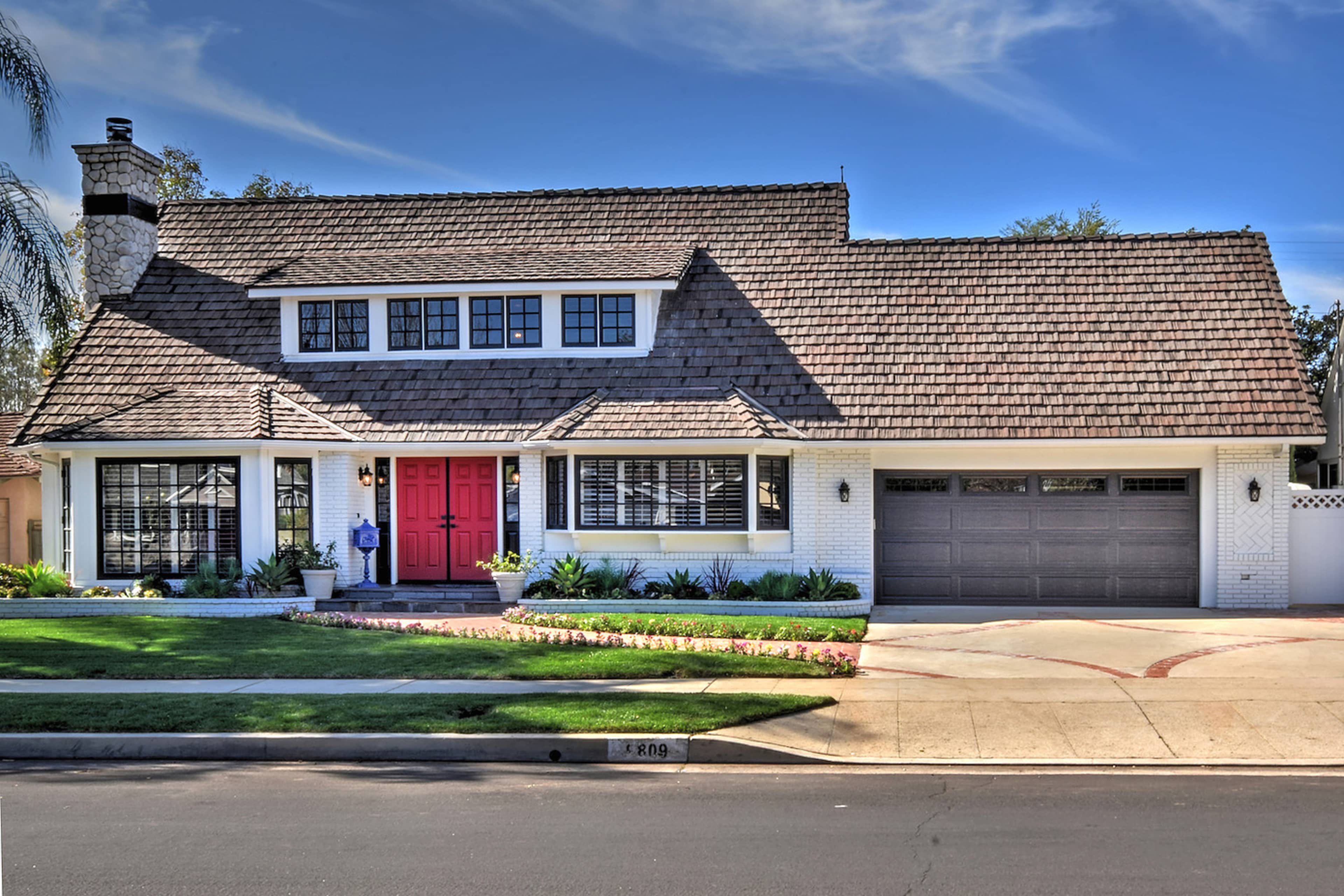 A two-story house with a red front door, a sloped roof, and a two-car garage is situated on a suburban street.