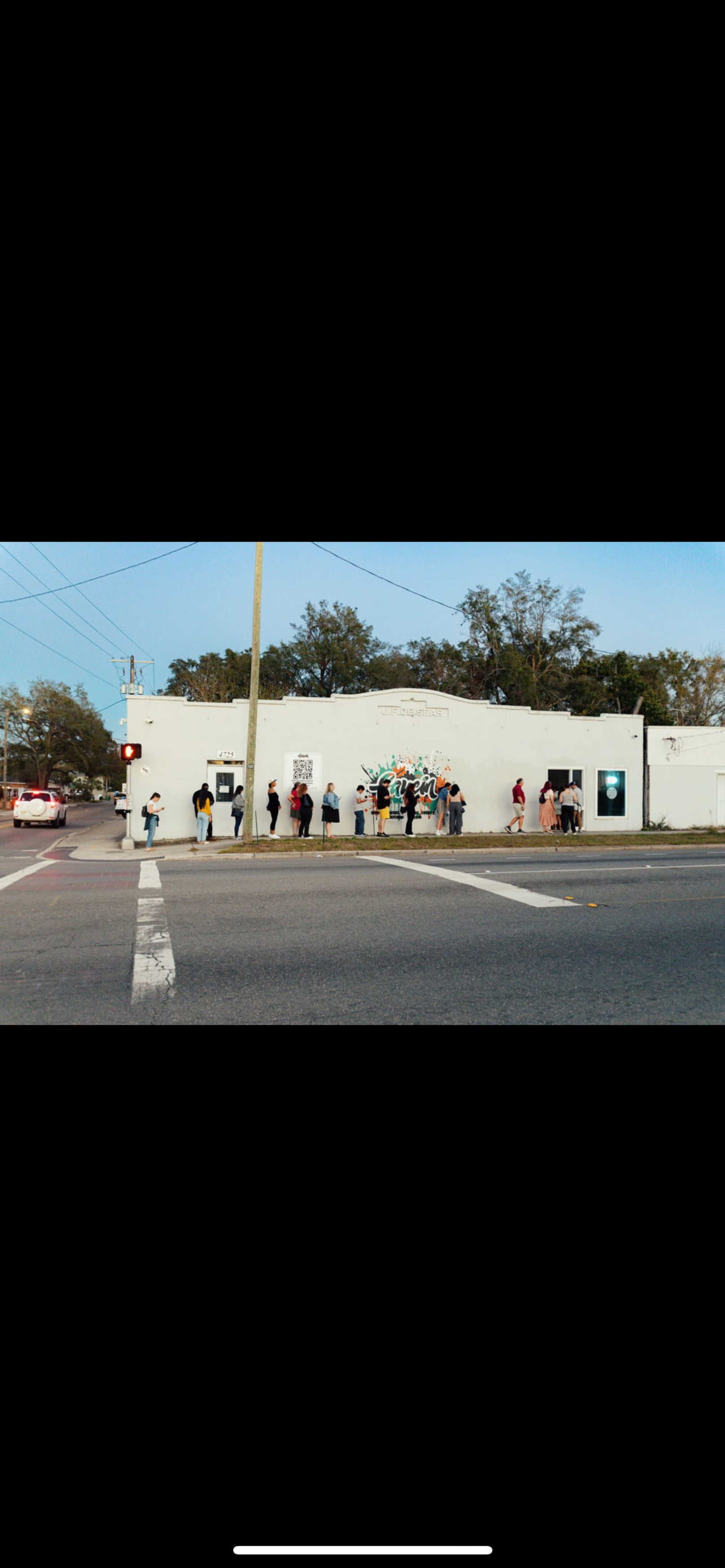 A group of people stands in line in front of a white building with colorful murals on its walls.