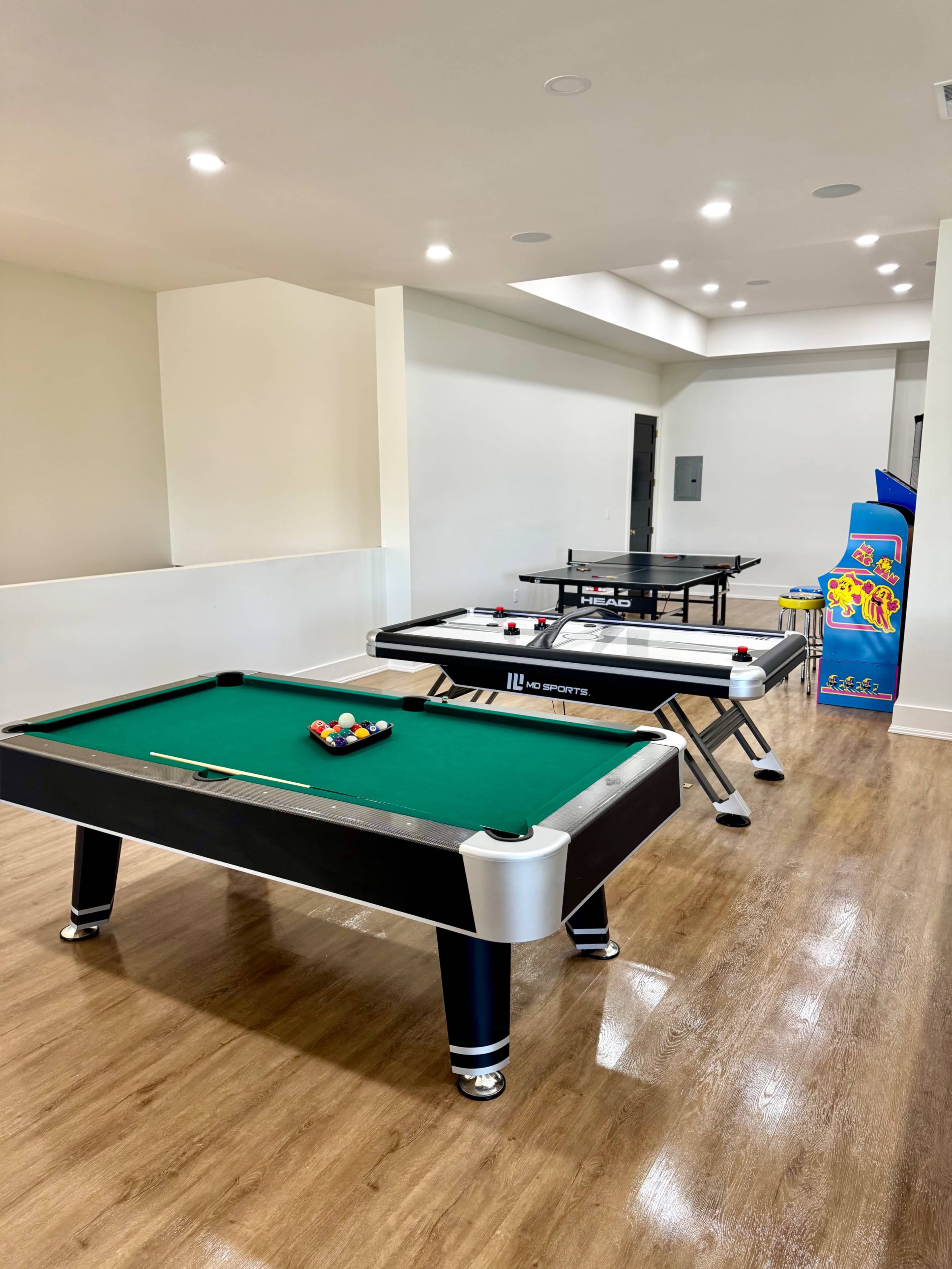 The image shows a recreational room with a pool table, a ping pong table, and an arcade machine.