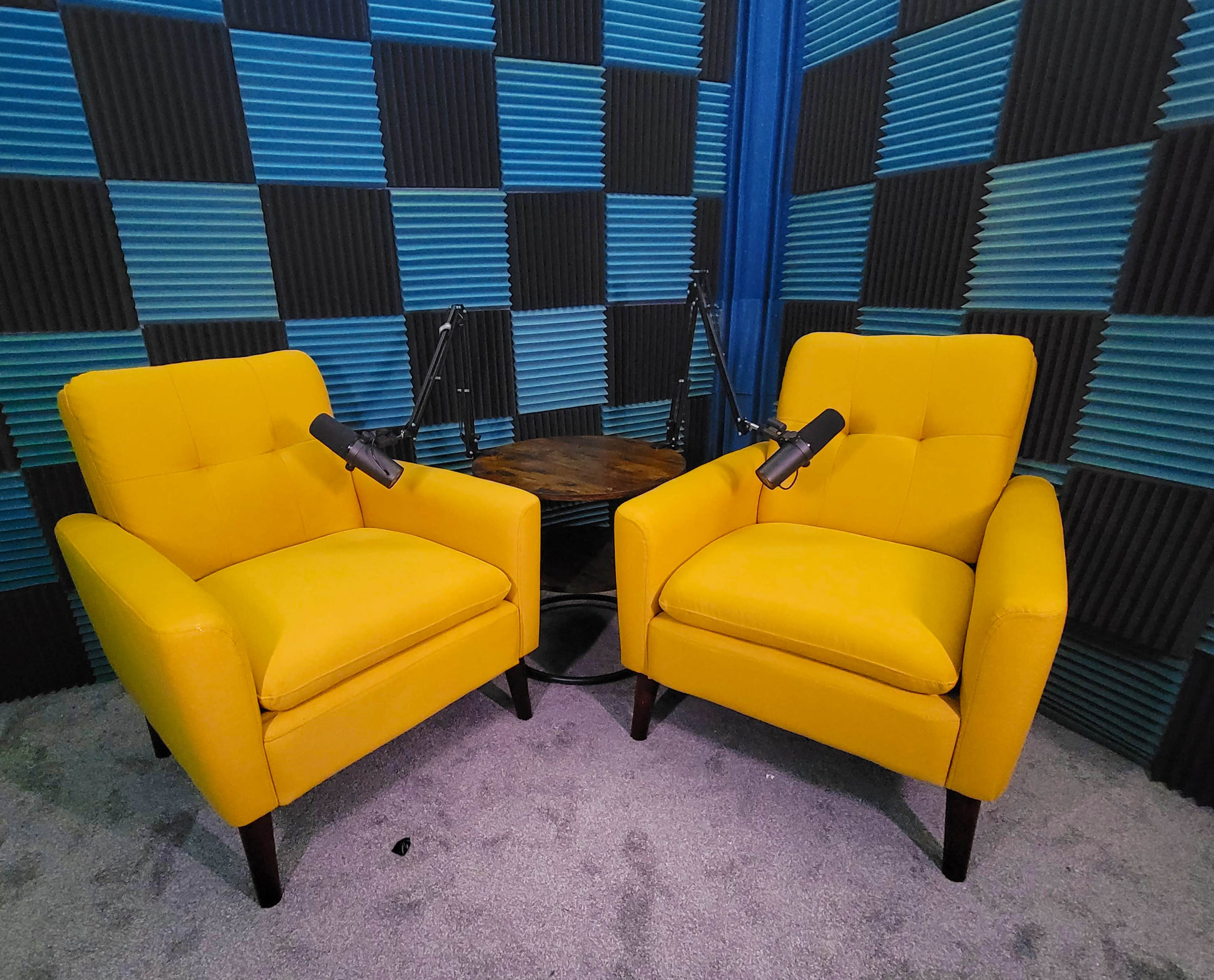 Two yellow armchairs facing each other, positioned next to a small wooden table, with soundproofing foam panels in shades of blue and black in the background.