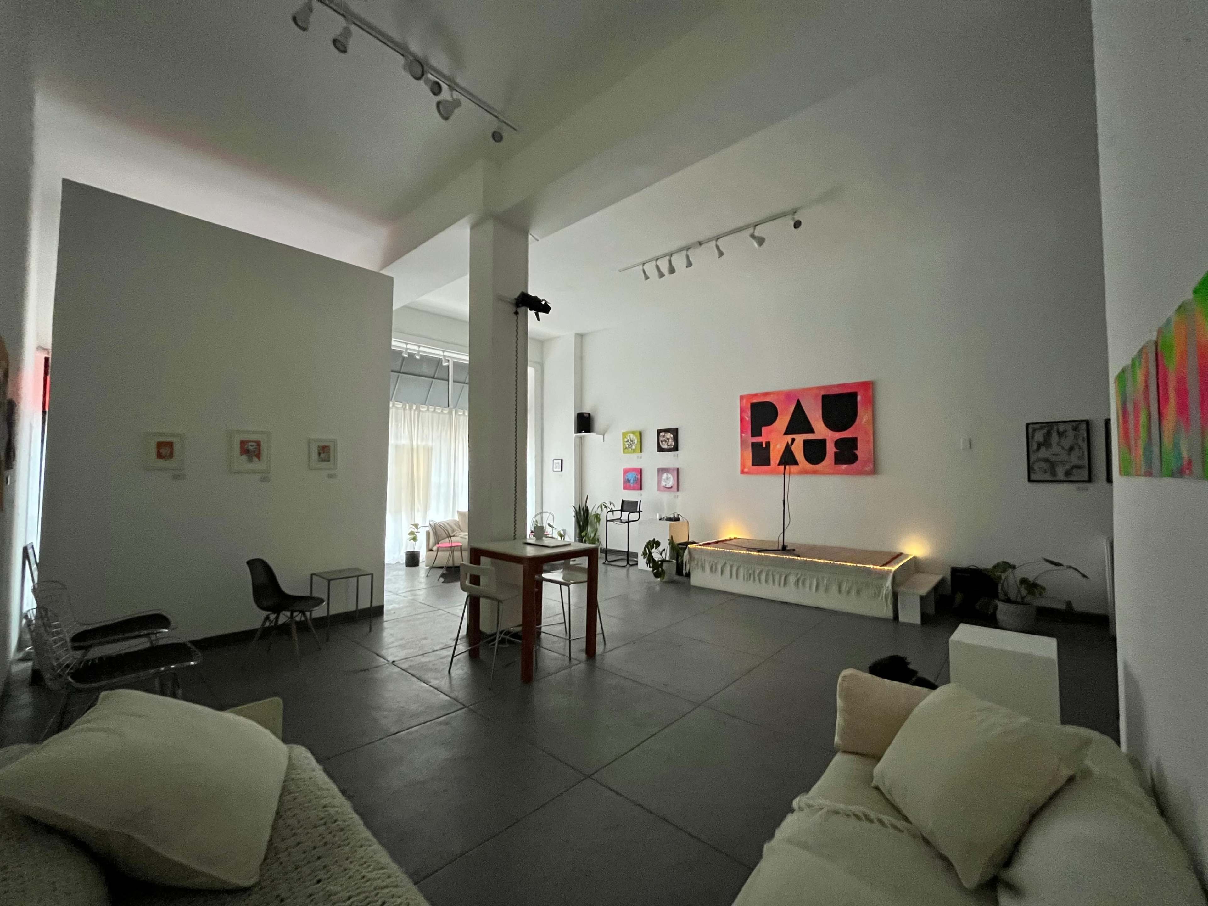 A spacious, modern art studio featuring a mix of seating, a long bench, and various artworks displayed on the white walls.