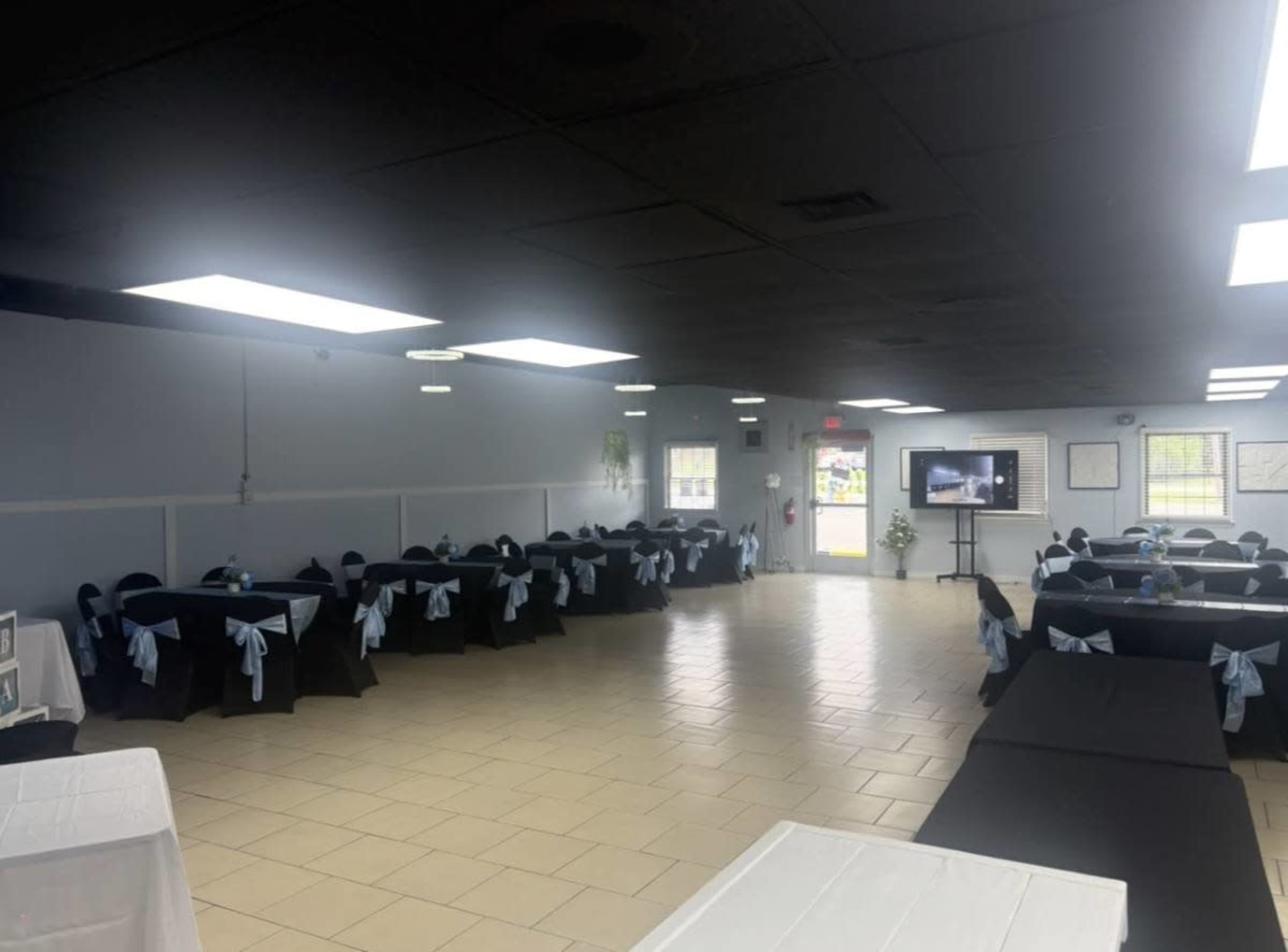 The image shows a spacious banquet hall with black and white table settings adorned with light blue bows on the chairs.