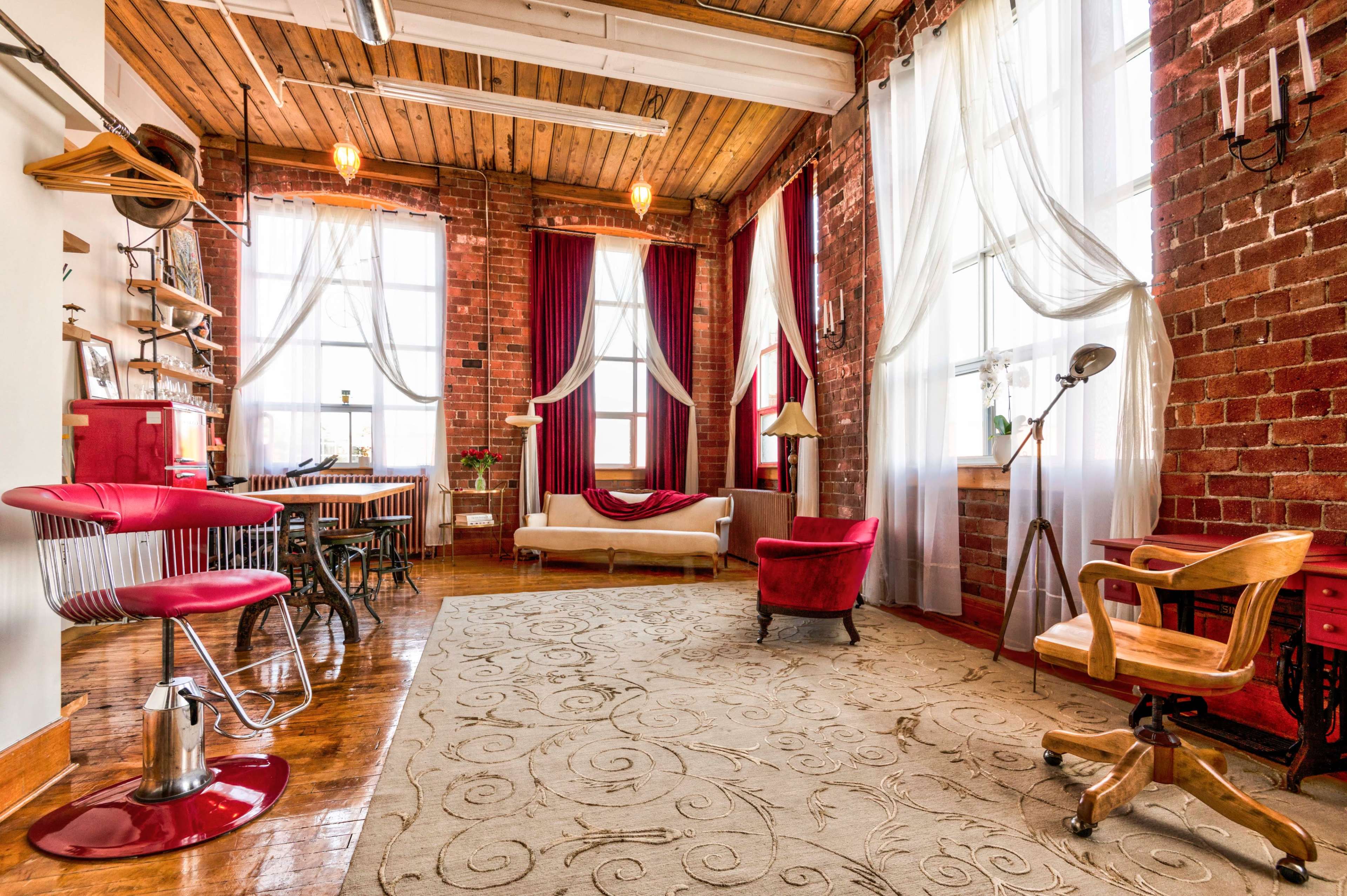 A spacious industrial-style room with exposed brick walls, large windows, and a mix of modern and vintage furniture.