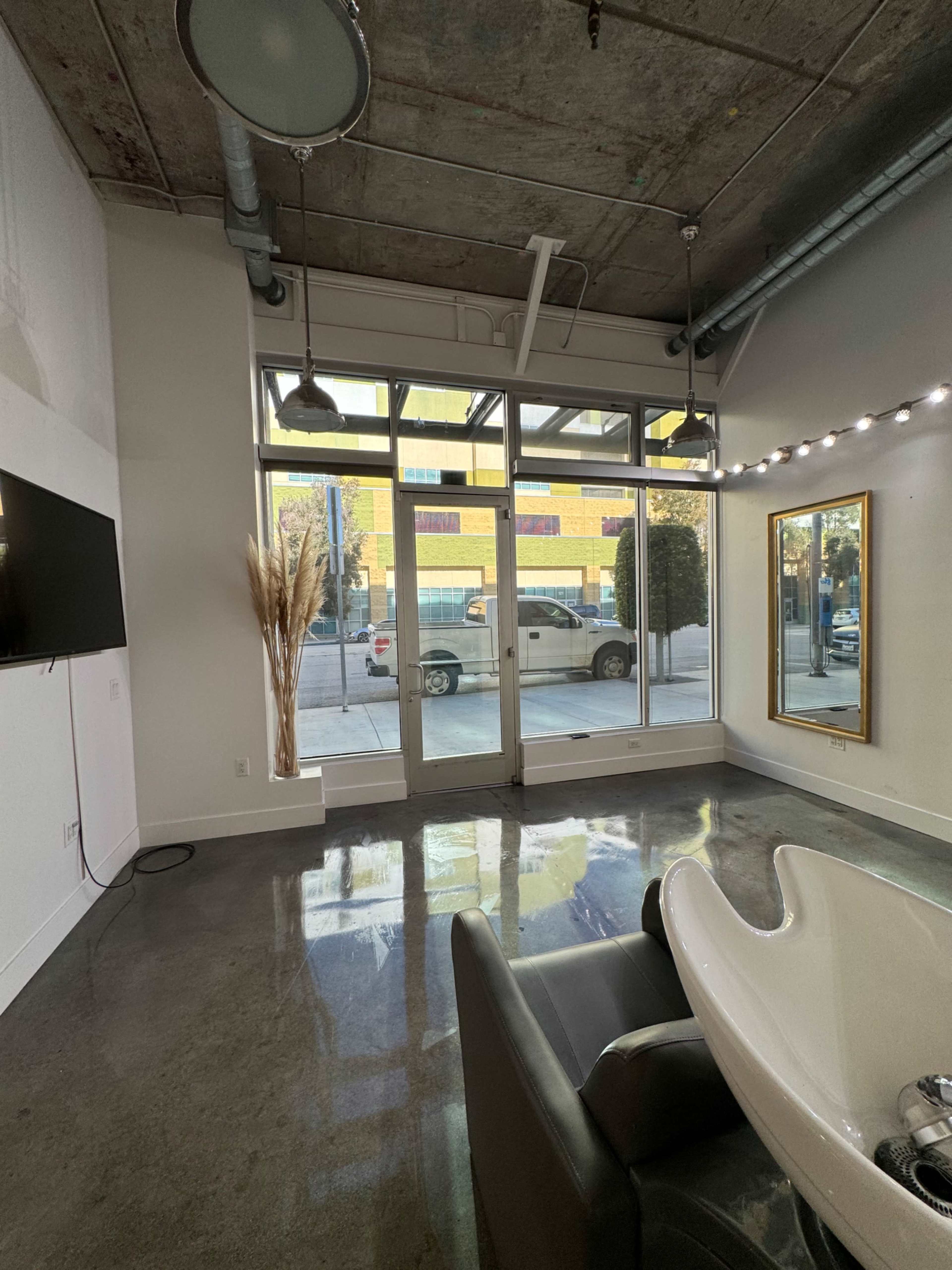 A modern salon interior featuring a washing station, a large mirror, and a view of a street through glass doors.