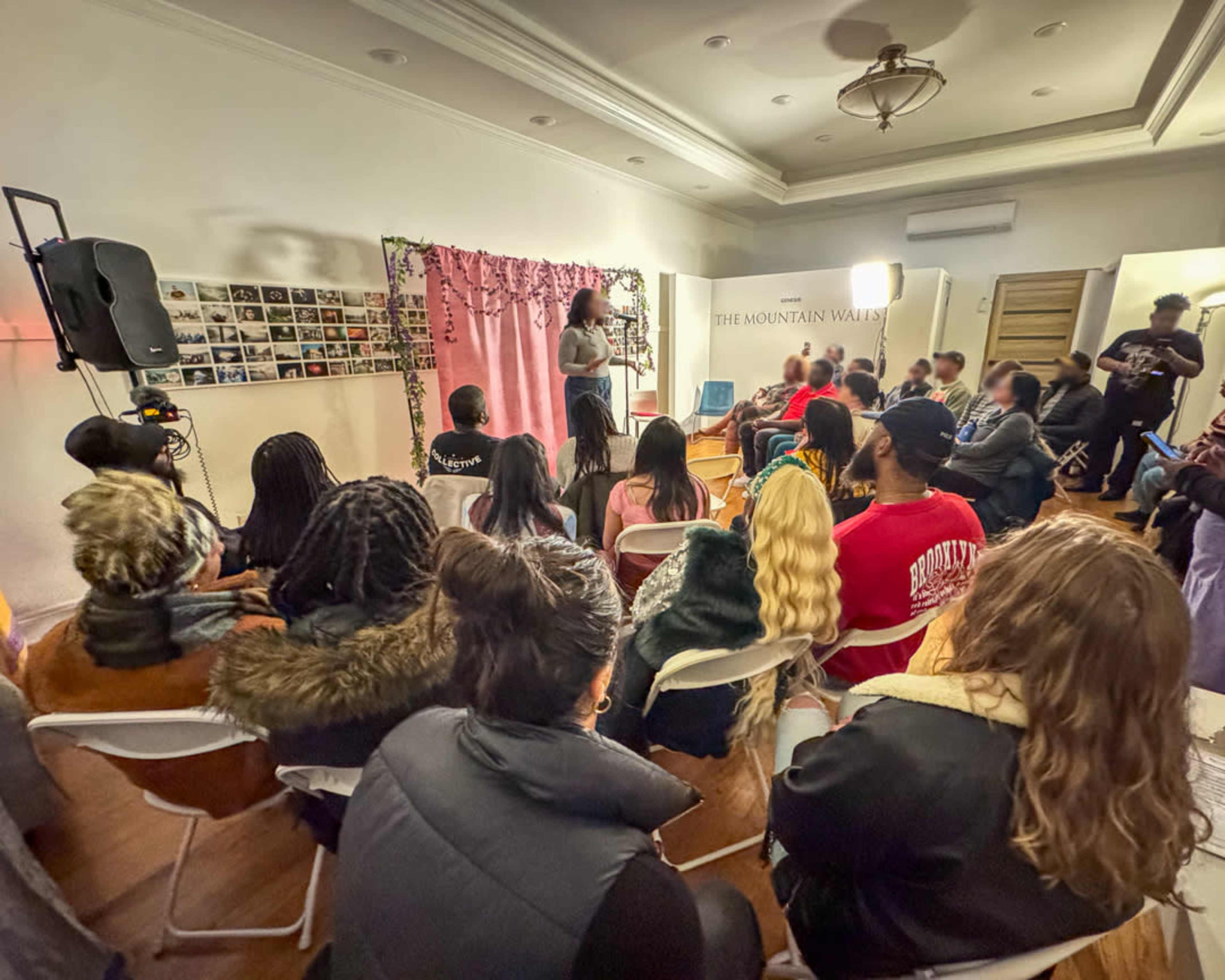 A diverse audience sits in a room, attentively listening to a speaker in front of a decorated backdrop.