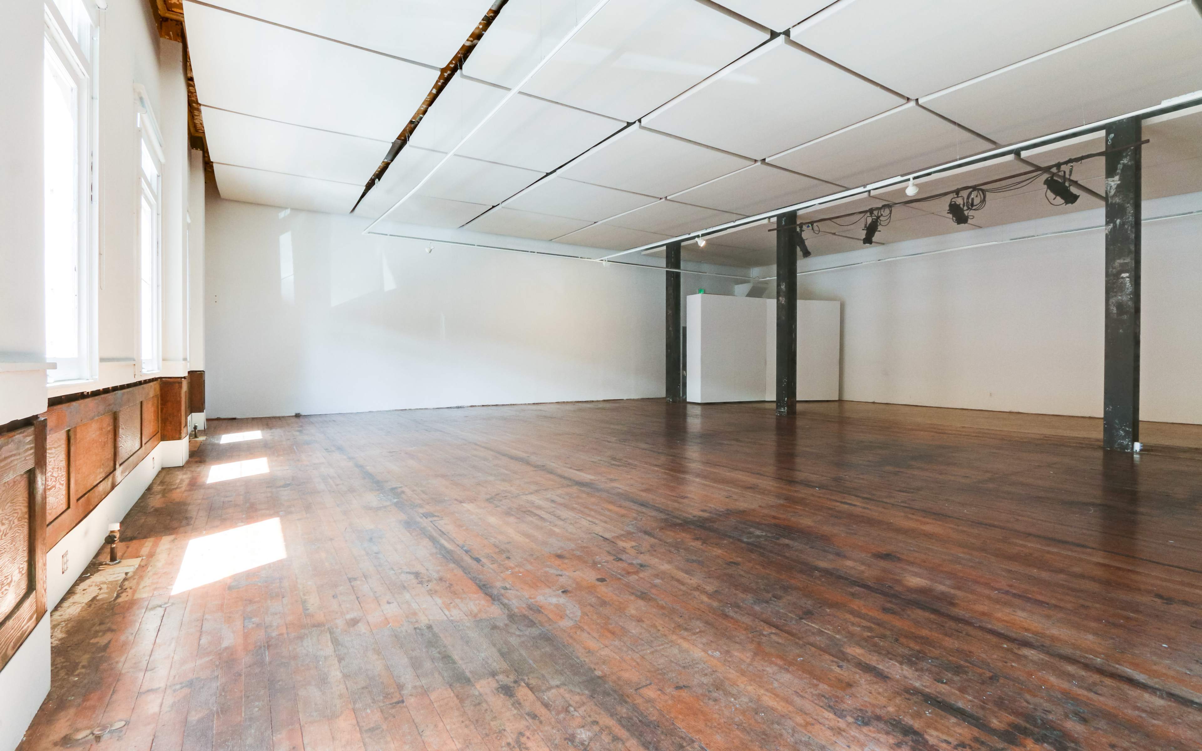 A spacious, empty room with wooden floors, large windows allowing natural light, and a minimalist design.