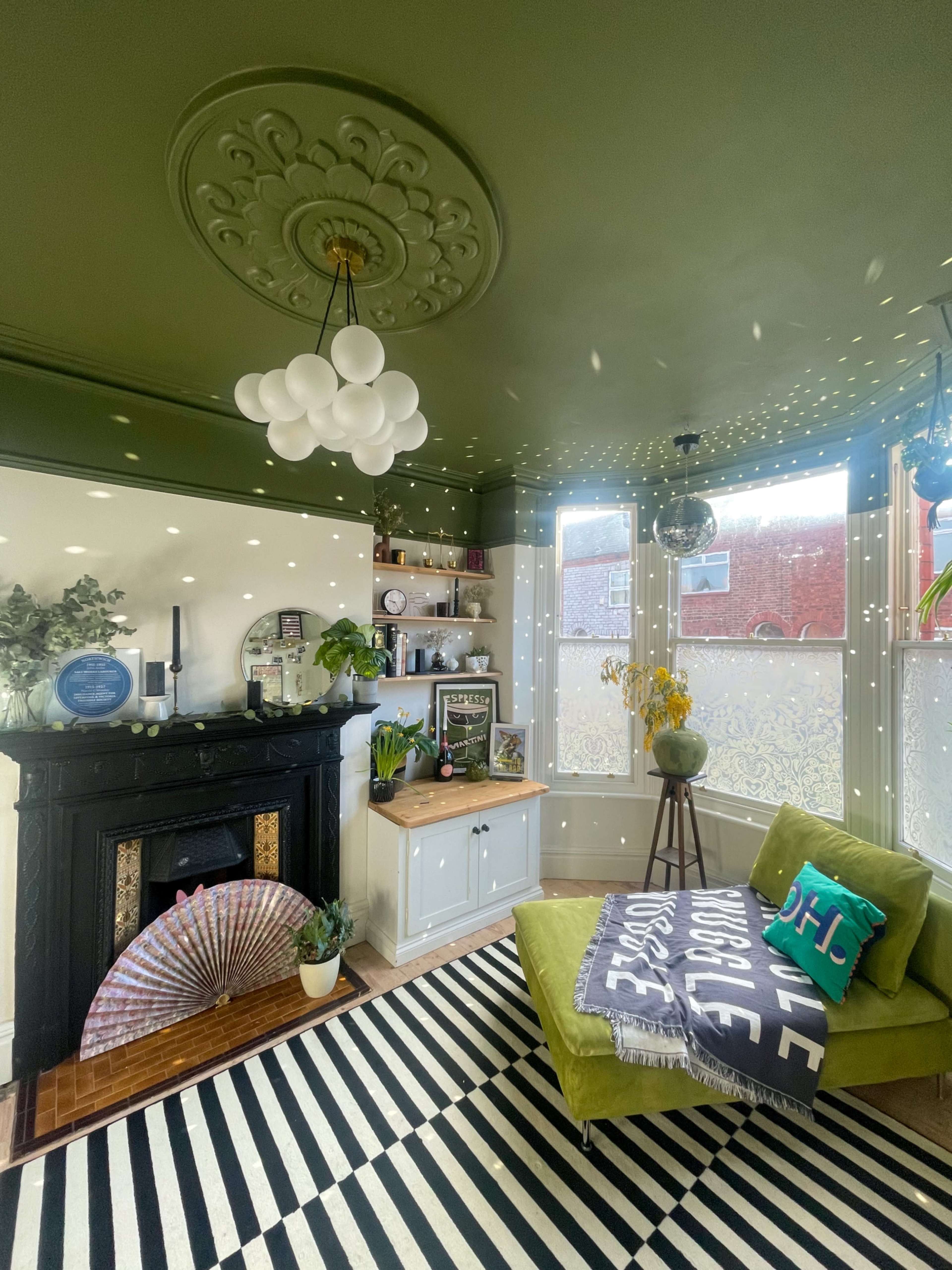 A cozy living room featuring a green ceiling, a patterned black and white rug, a decorative fireplace, and a chaise lounge in bright green.