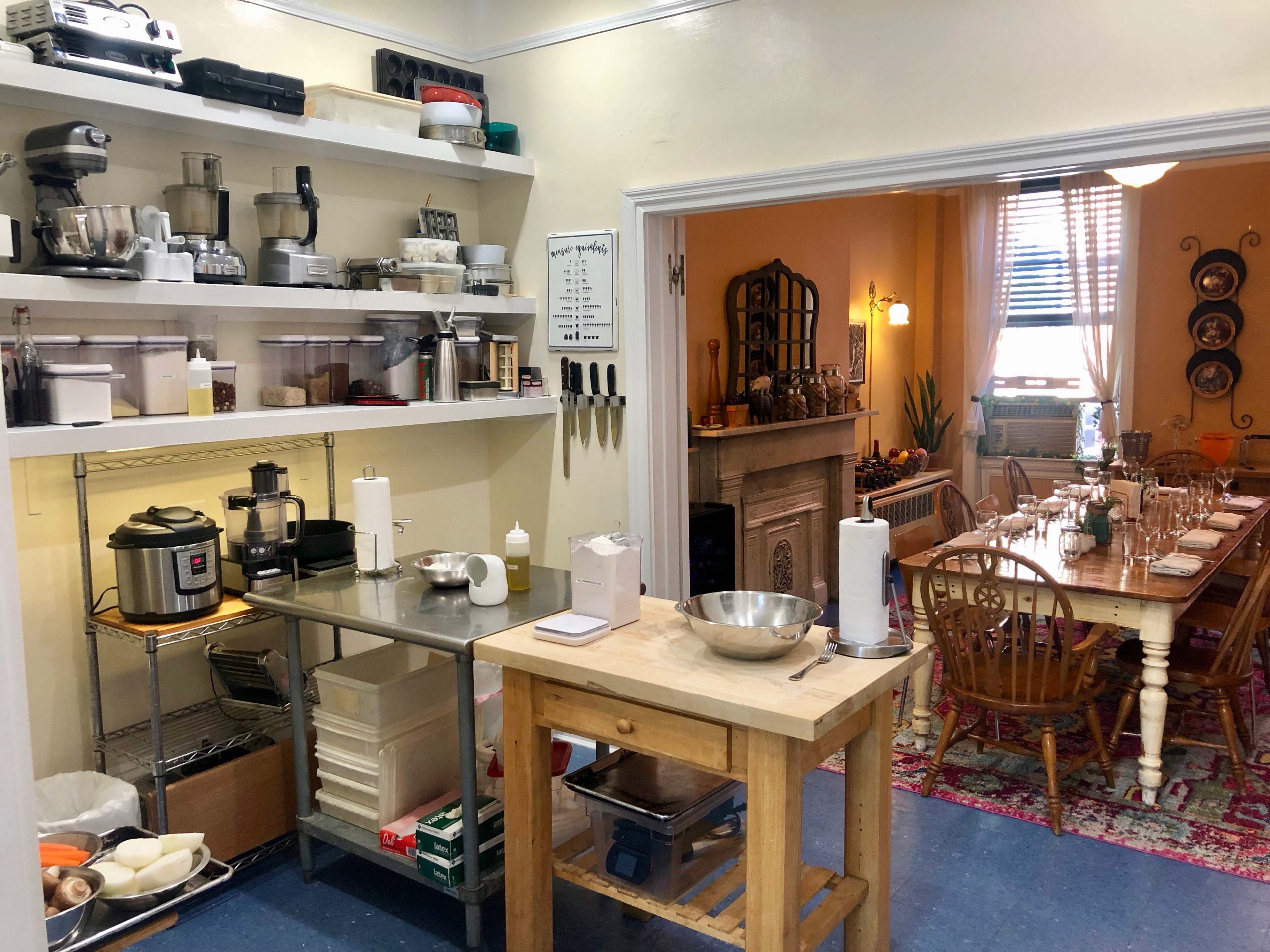 A kitchen area on the left with various appliances and utensils, and a dining area to the right featuring a wooden table set for a meal.