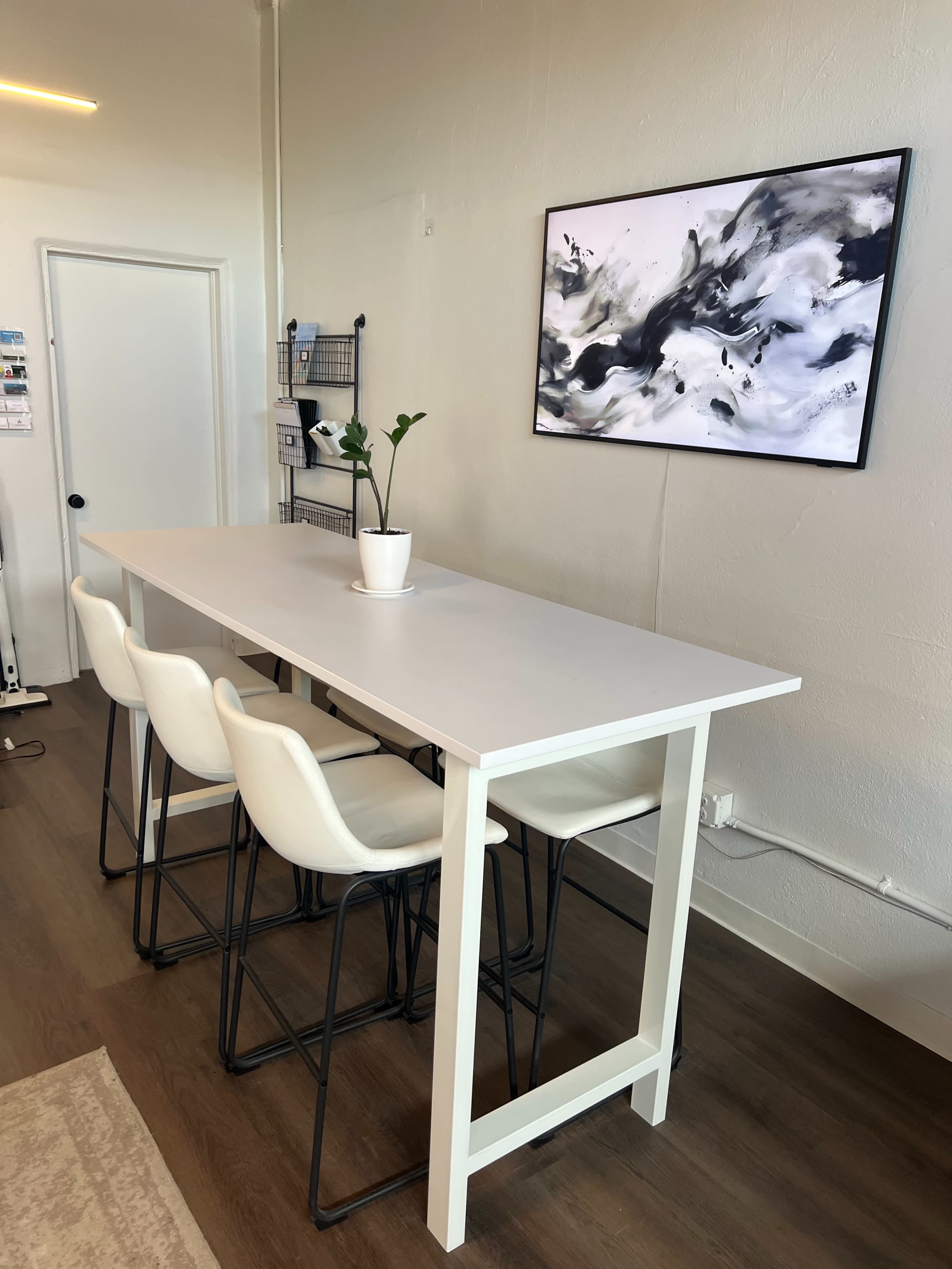 A modern white table with four black and white bar stools is set against a light-colored wall, featuring a large abstract artwork above it.