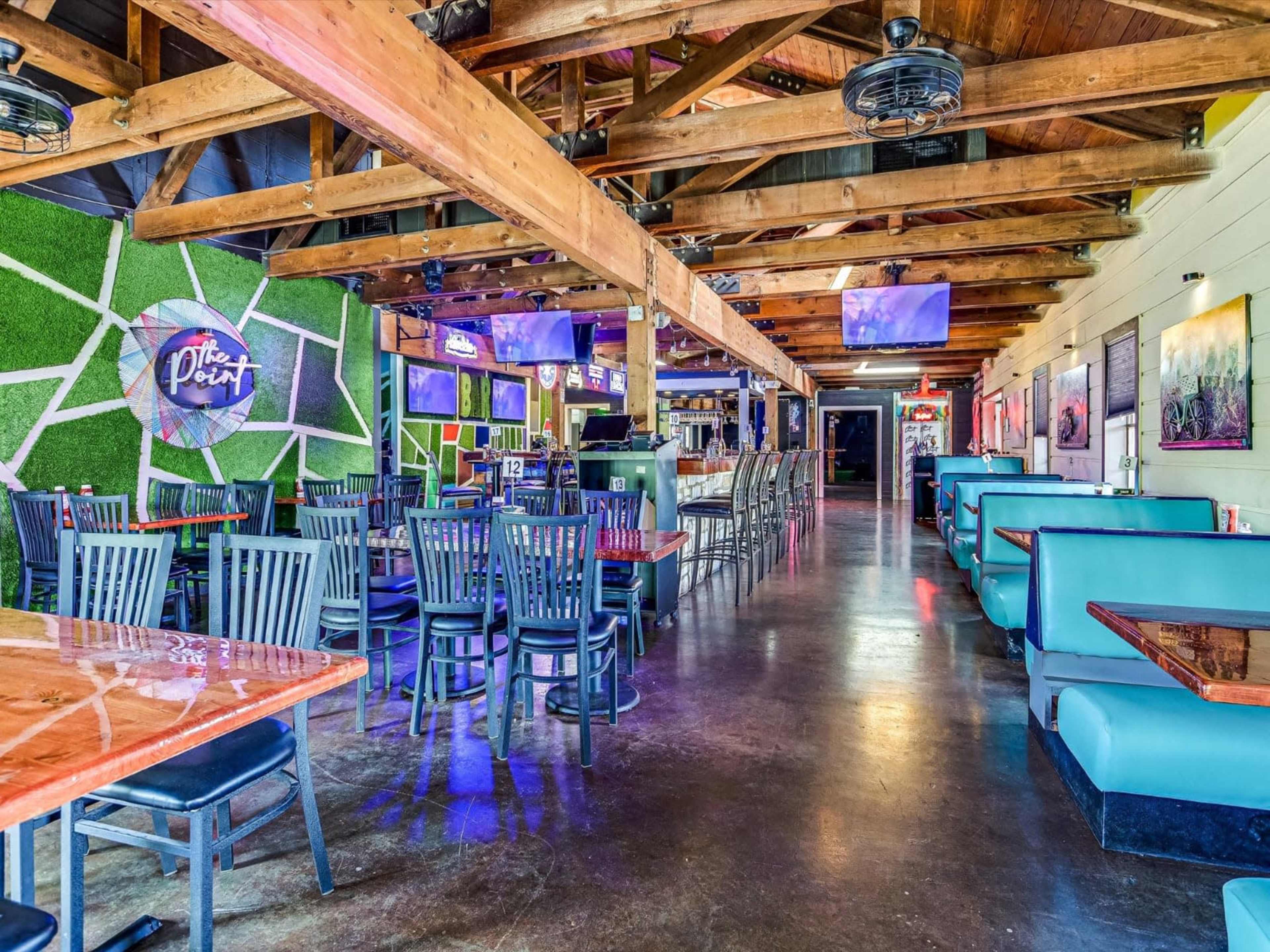 The image shows a spacious restaurant interior with wooden beams, multiple seating areas, and several large screens mounted on the walls.