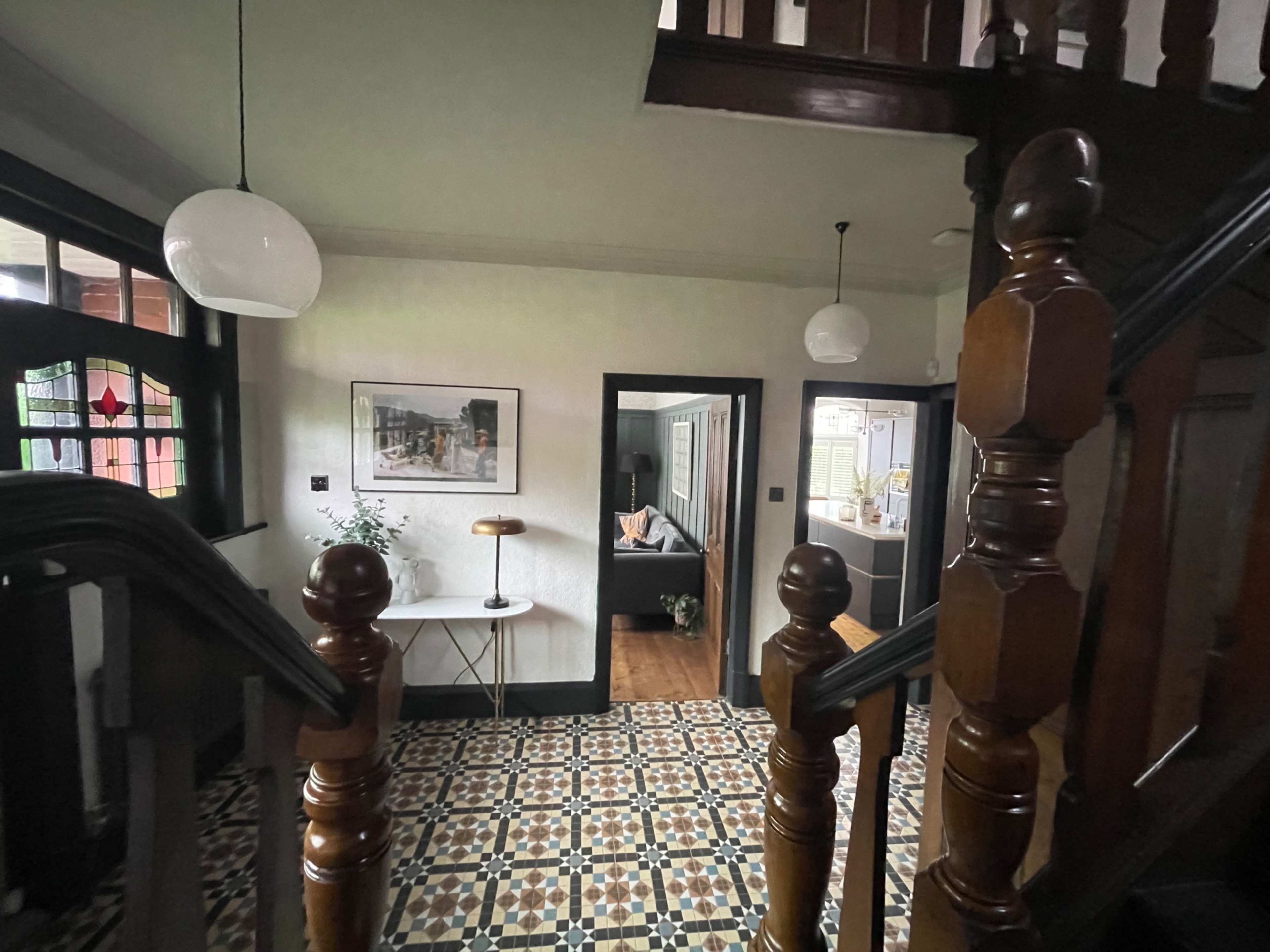 The image shows a hallway with a patterned tiled floor, a staircase with wooden banisters, and doorways leading to other rooms.