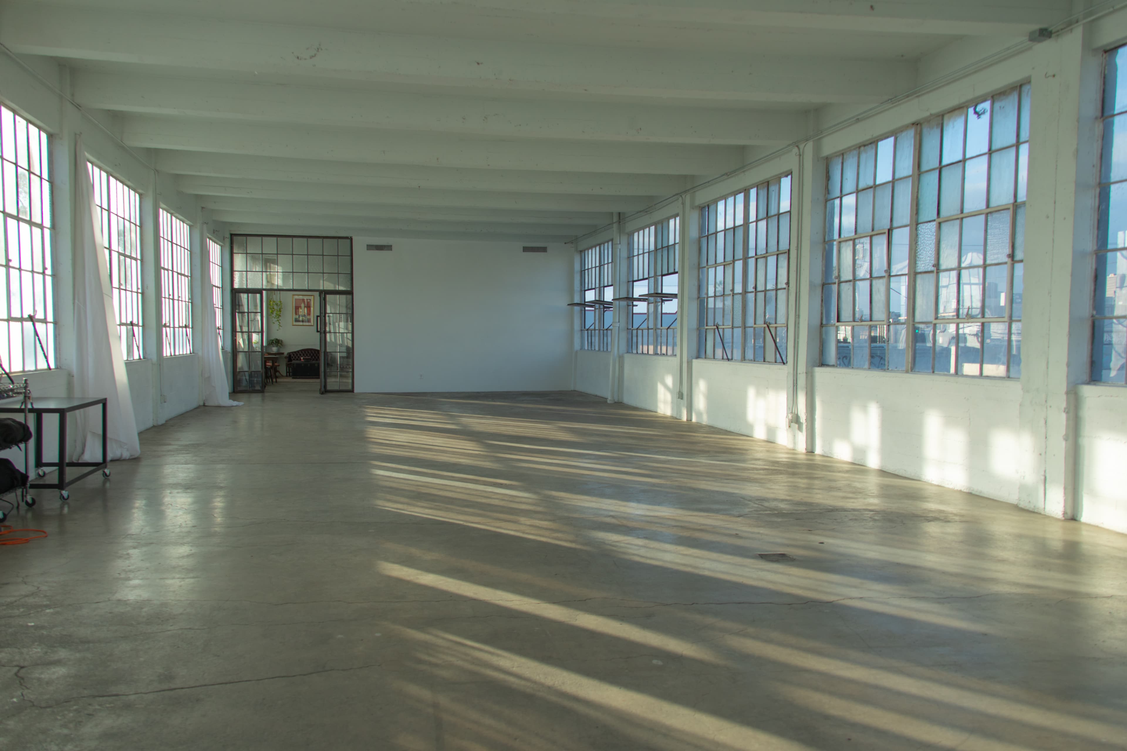 A spacious, empty room with large windows allowing natural light to fill the space, and concrete flooring.