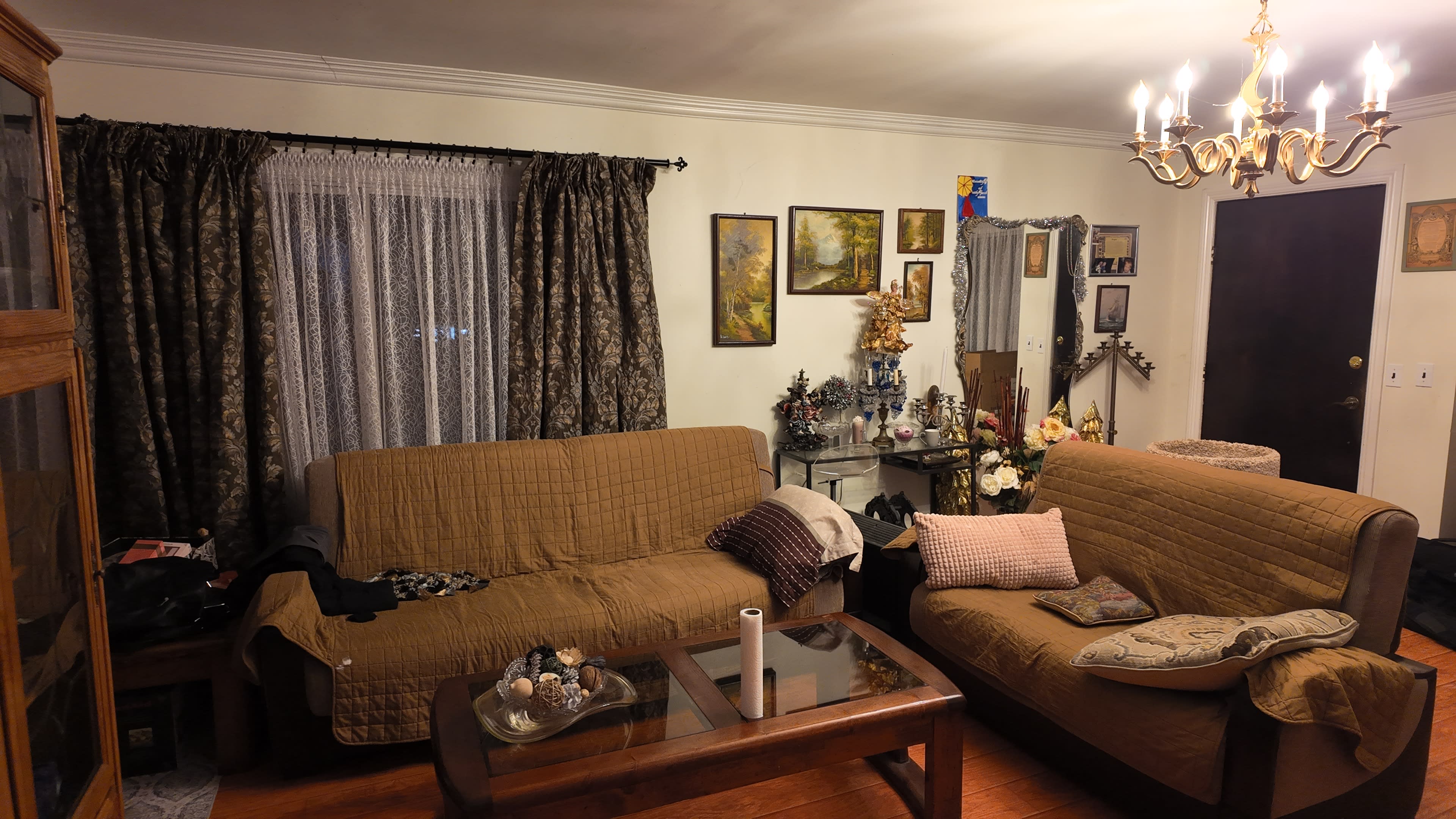 The living room features two brown sofas, a glass coffee table, and a decorative display with artwork and a chandelier overhead.