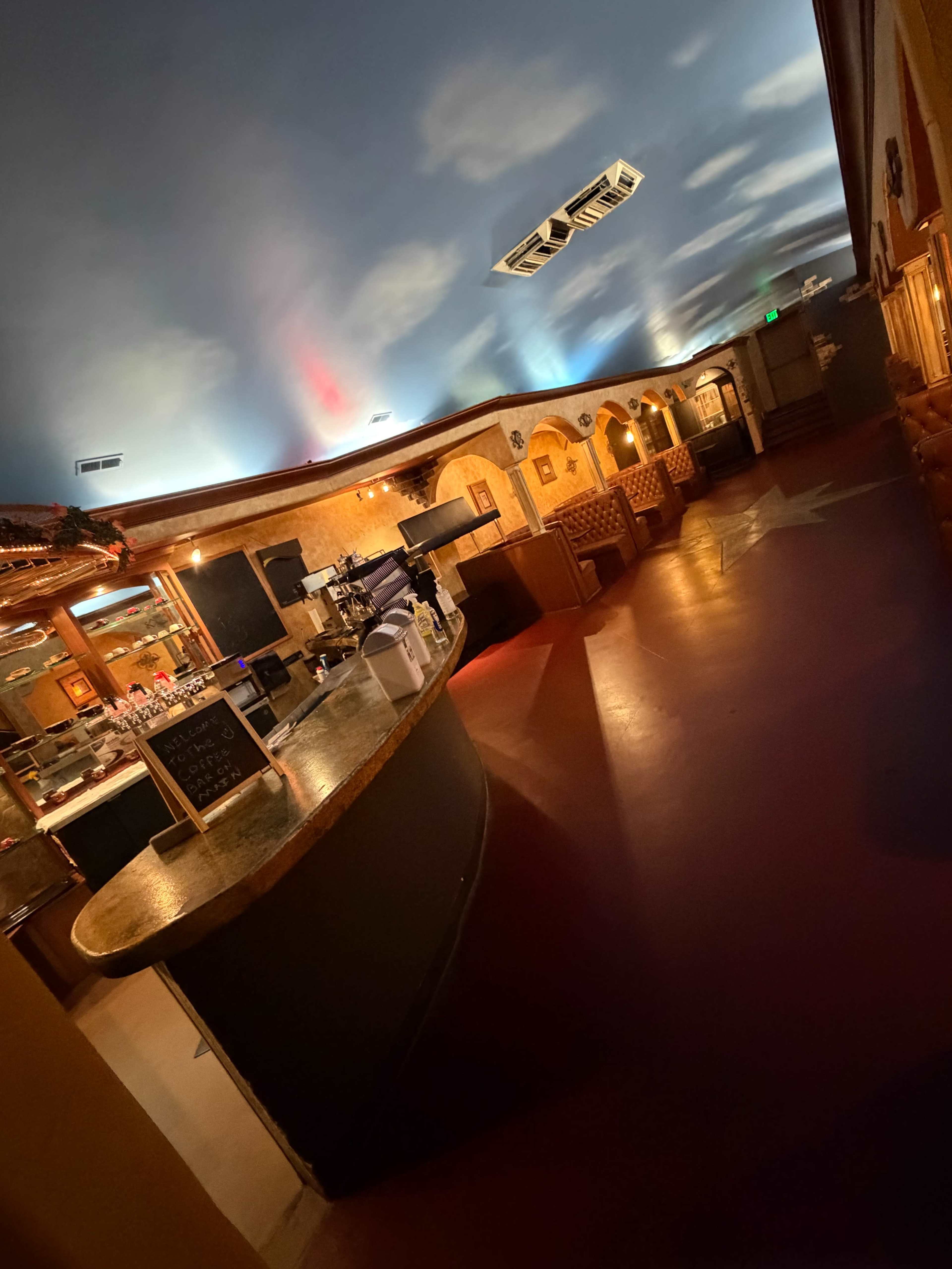 The image shows the interior of a restaurant or bar with a curved counter, booths along the walls, and colorful lighting on the ceiling.