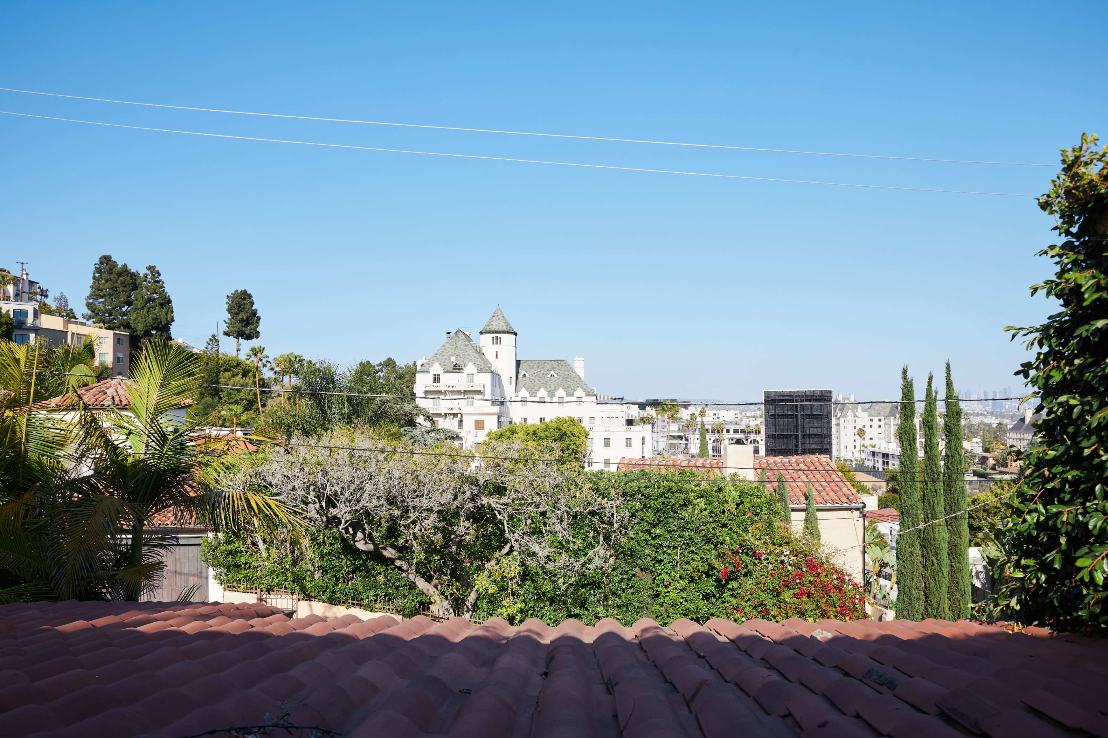 A view of a large building with a tower, surrounded by greenery and houses, under a clear blue sky.