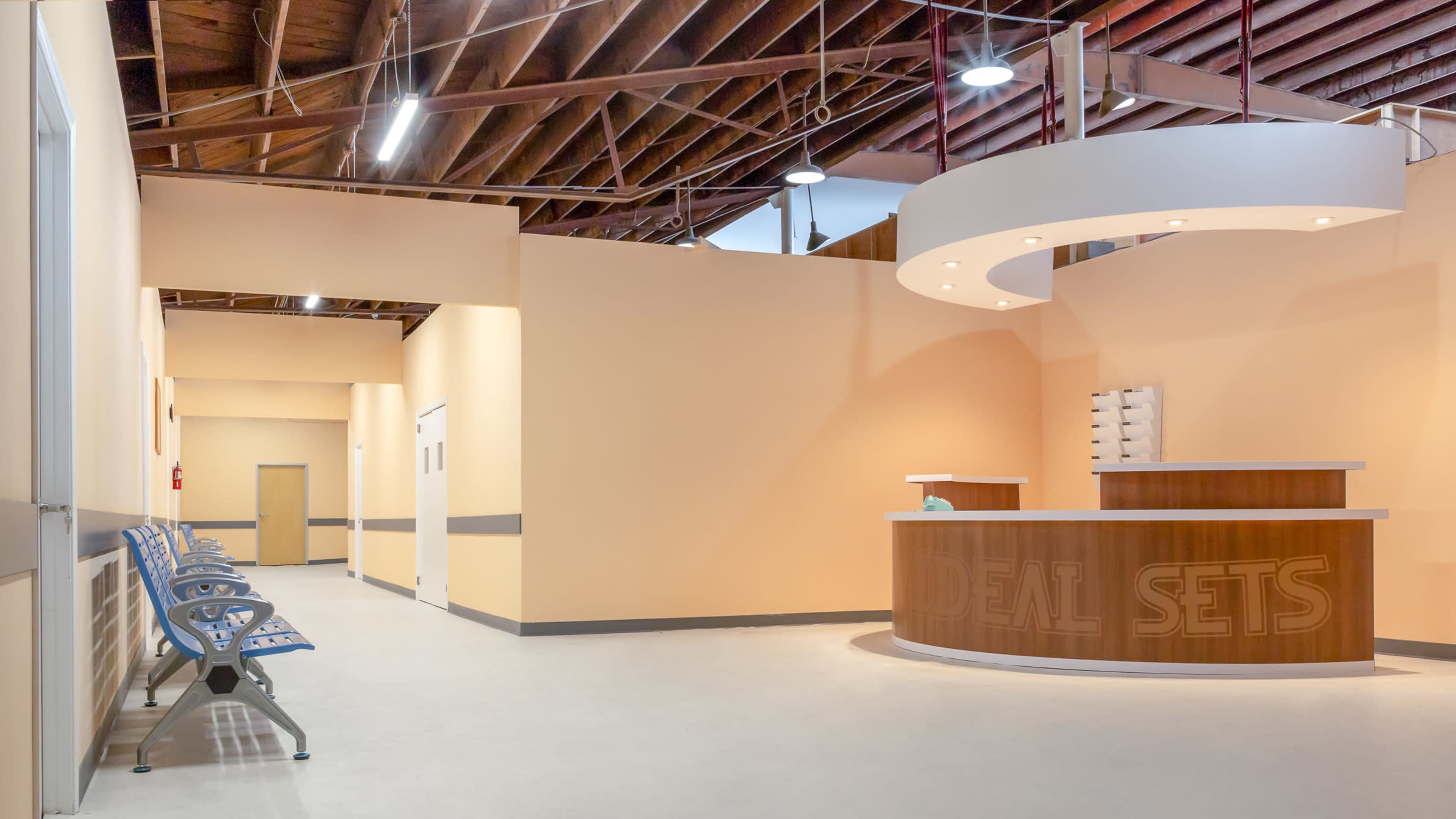 A modern reception area with a curved front desk and seating along the walls in a well-lit corridor.