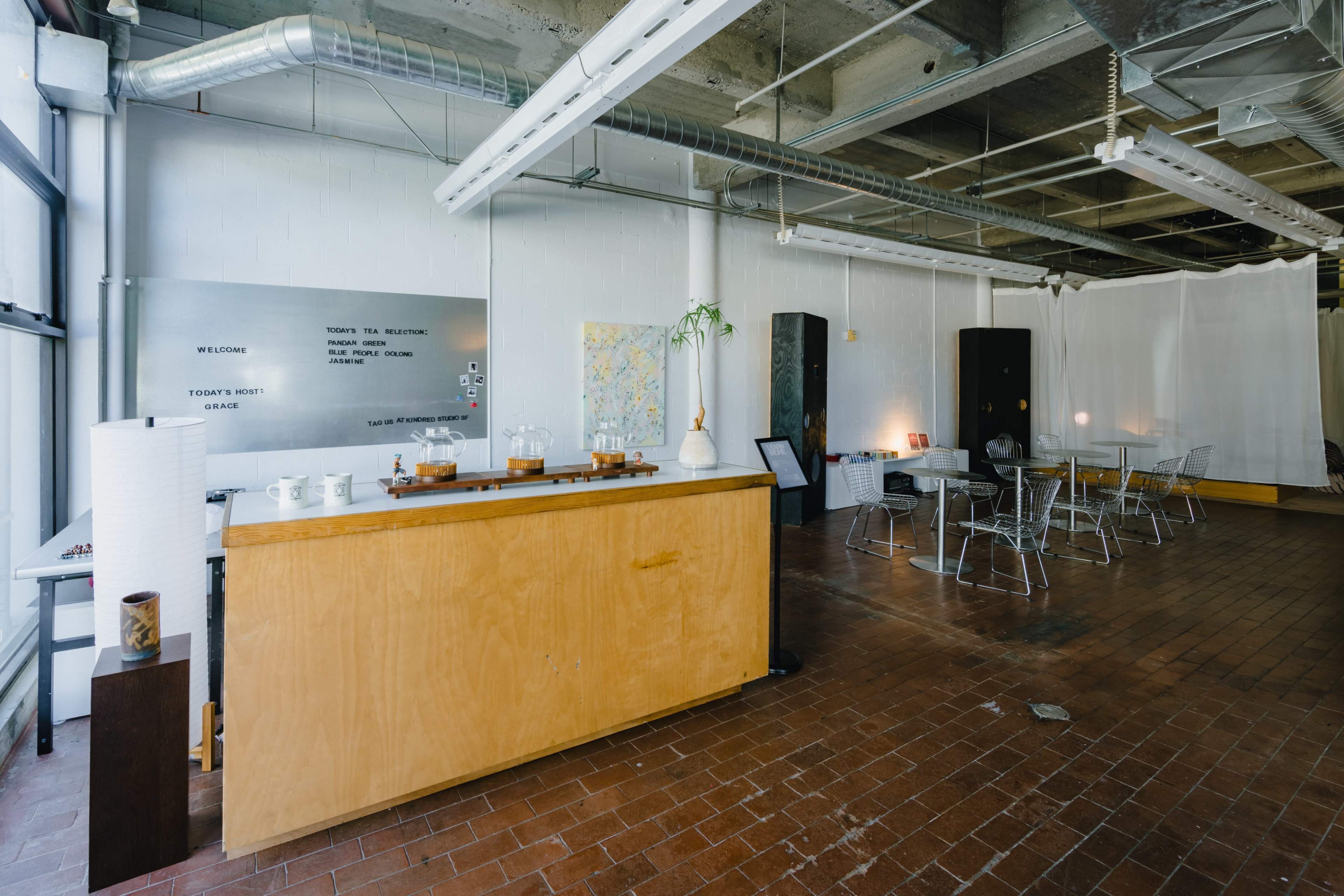 The image shows a spacious interior of a cafe or meeting area with wooden furniture, a service counter, and tables set up for patrons.