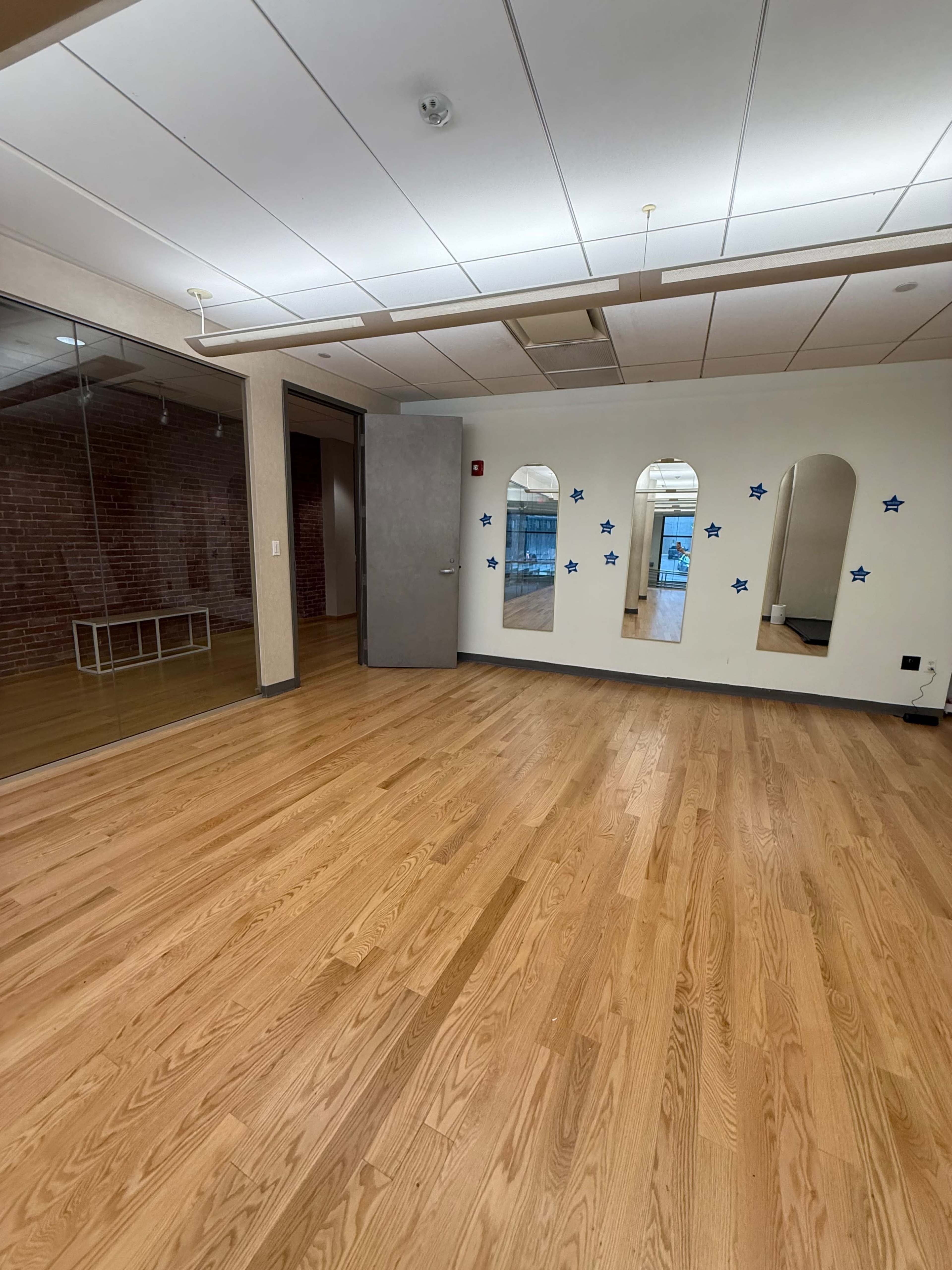 The image shows an empty room with wooden floors, a large glass wall on one side, and three mirrored arches adorned with blue stars on the opposite wall.