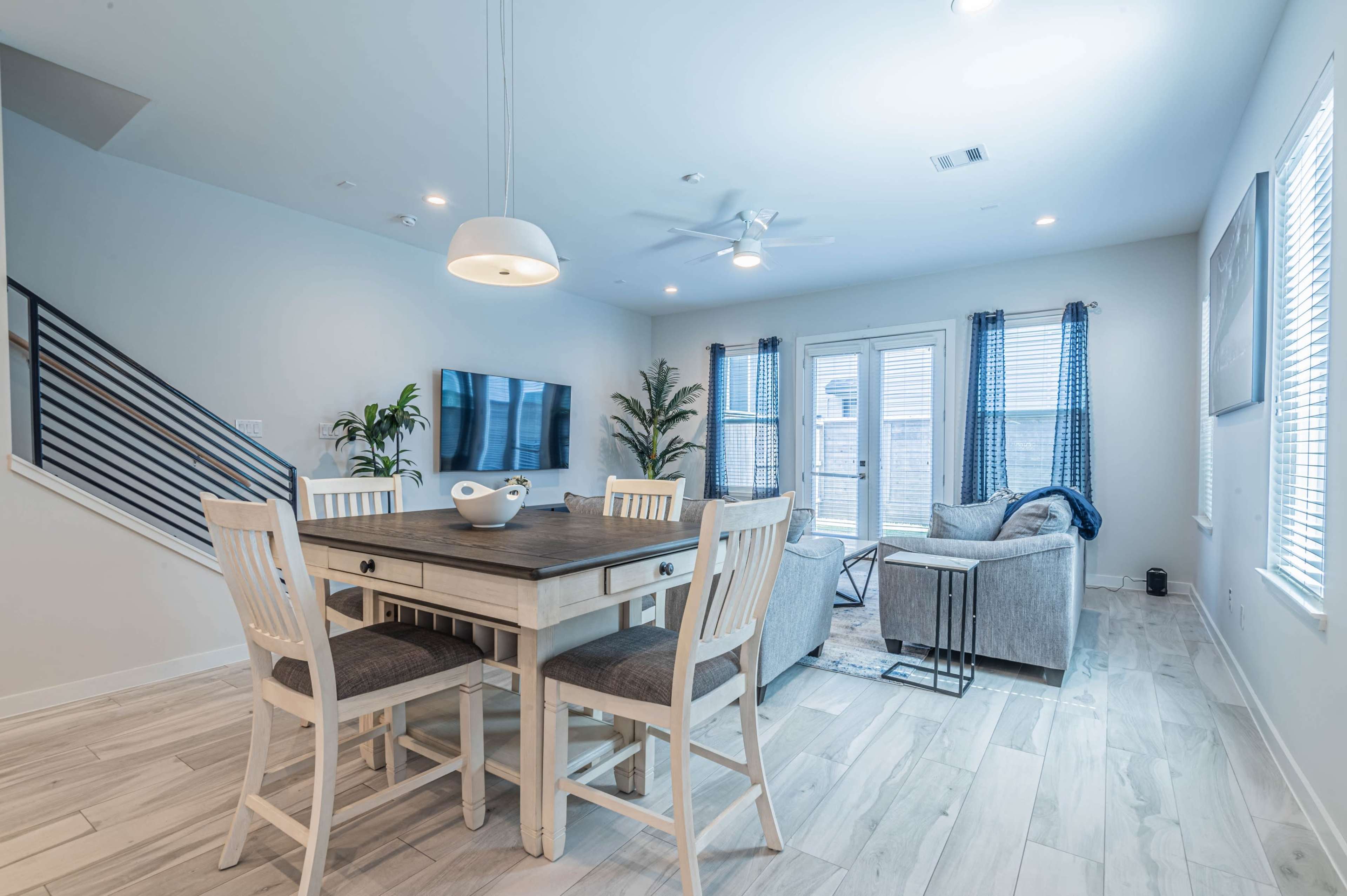 A modern living and dining area with a wooden table and chairs, sleek furniture, and large windows allowing natural light to enter.