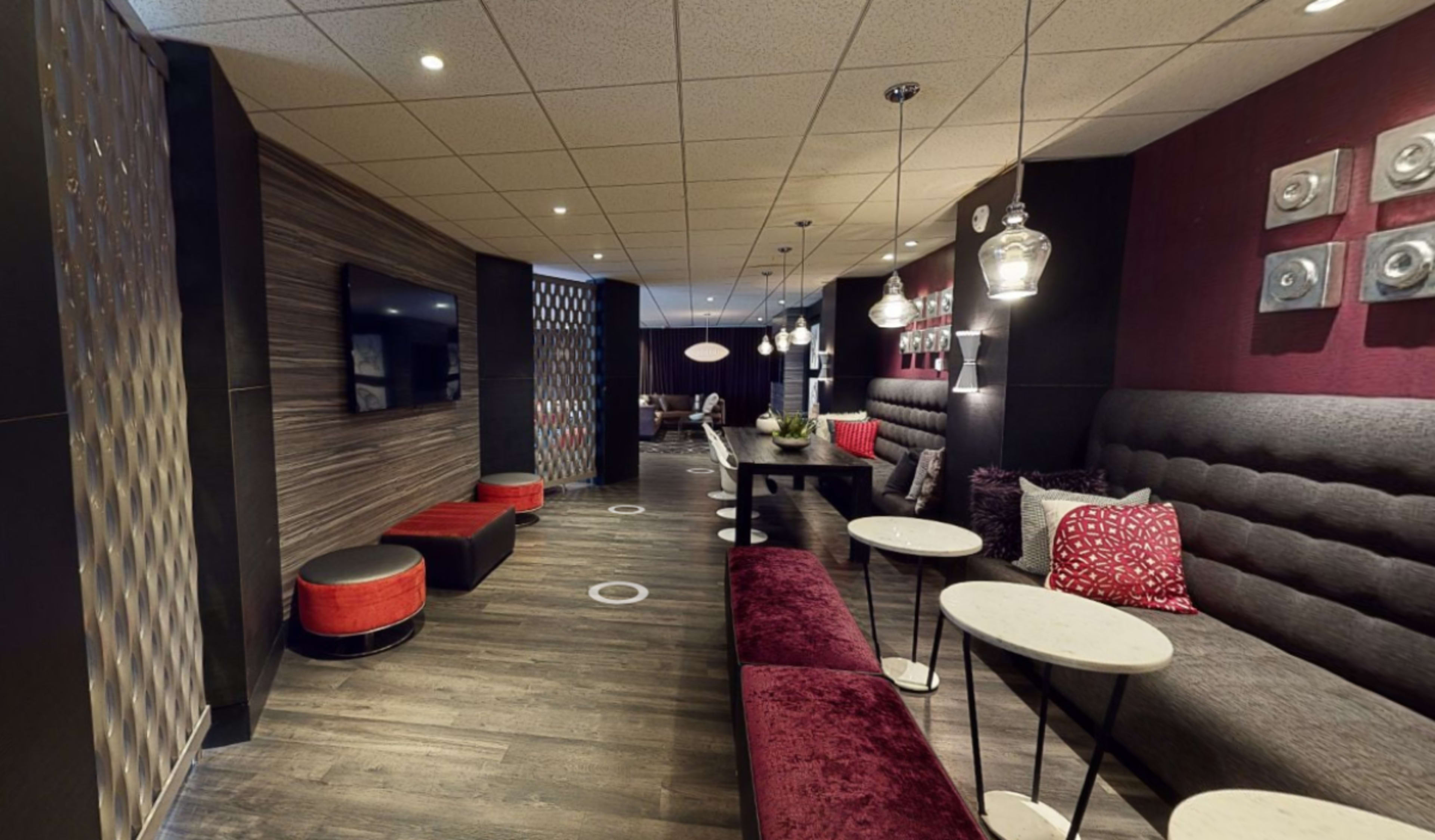 The image shows a modern lounge area with dark wood flooring, gray upholstered seating, and pendant lighting.
