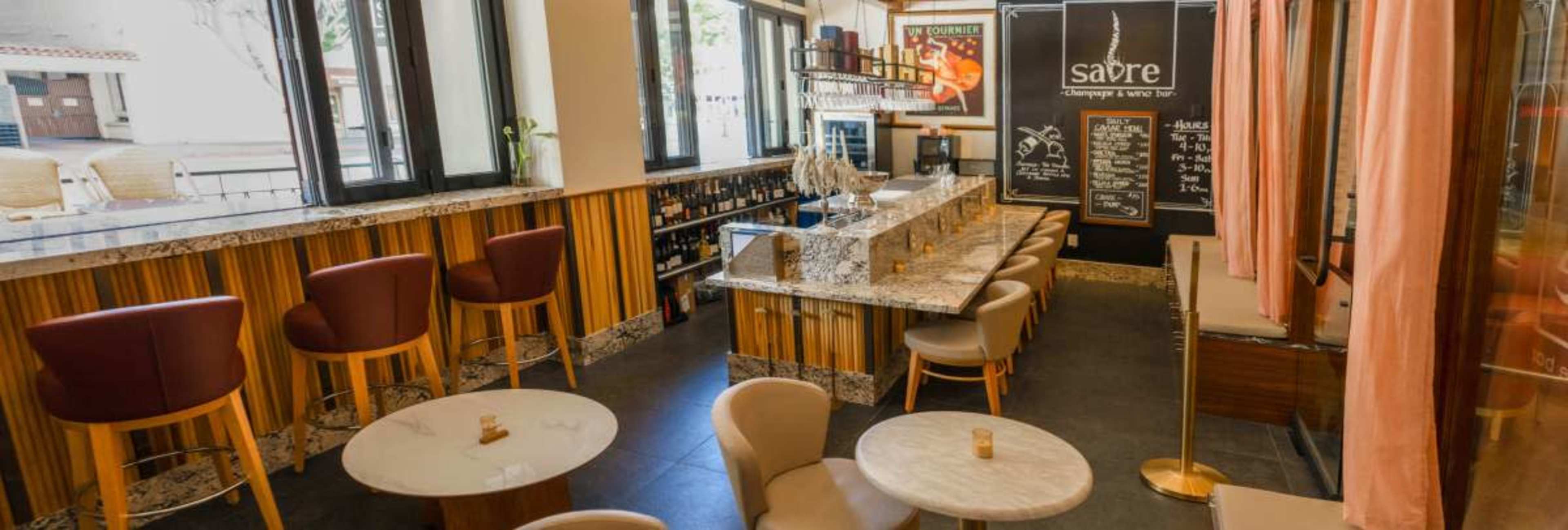 The image shows an upscale bar area with a marble countertop, high stools, and small tables, alongside a wall featuring a chalkboard menu.
