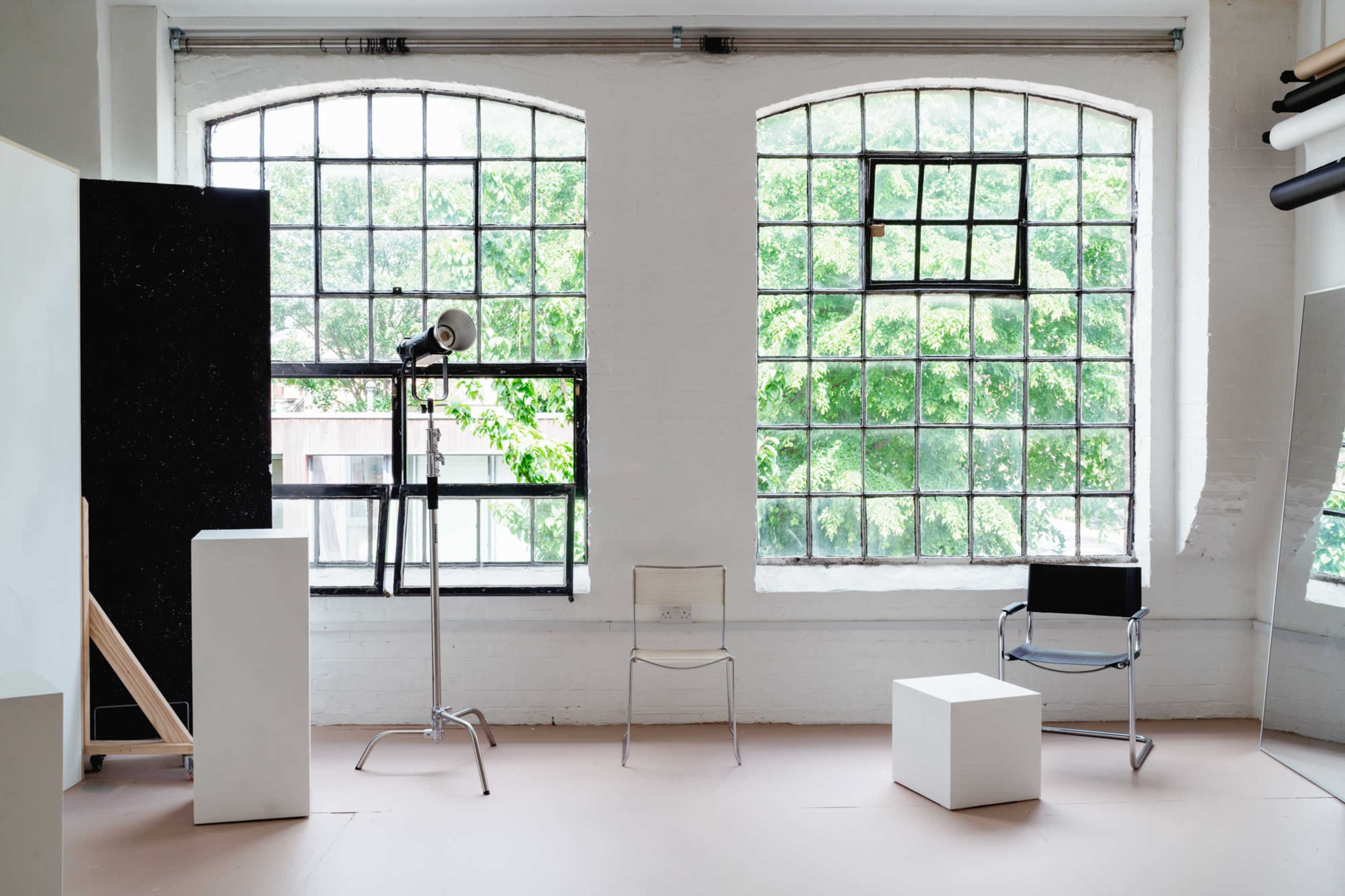 The scene features a bright room with large windows, two chairs, a lamp on a tripod, and several geometric white sculptures.