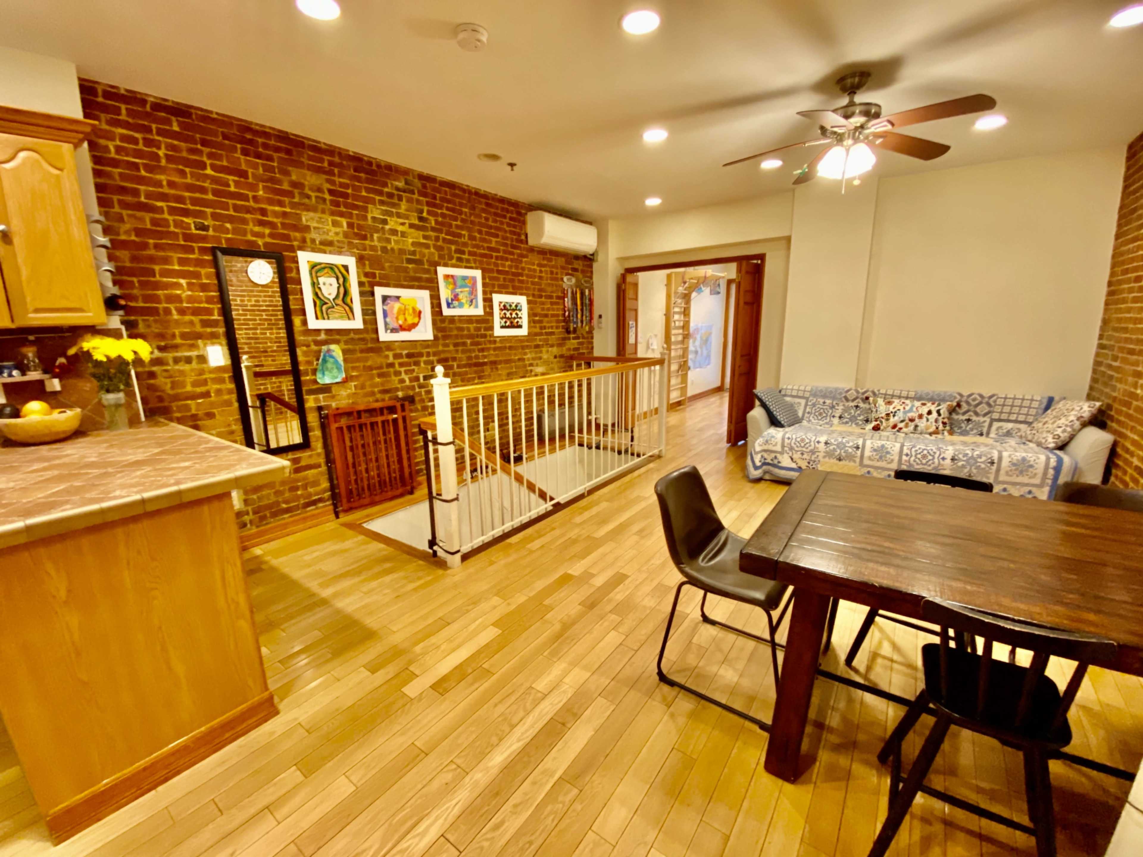 An open-concept living space featuring a kitchen area with wooden cabinets, a dining table, a seating area with a couch, and exposed brick walls.