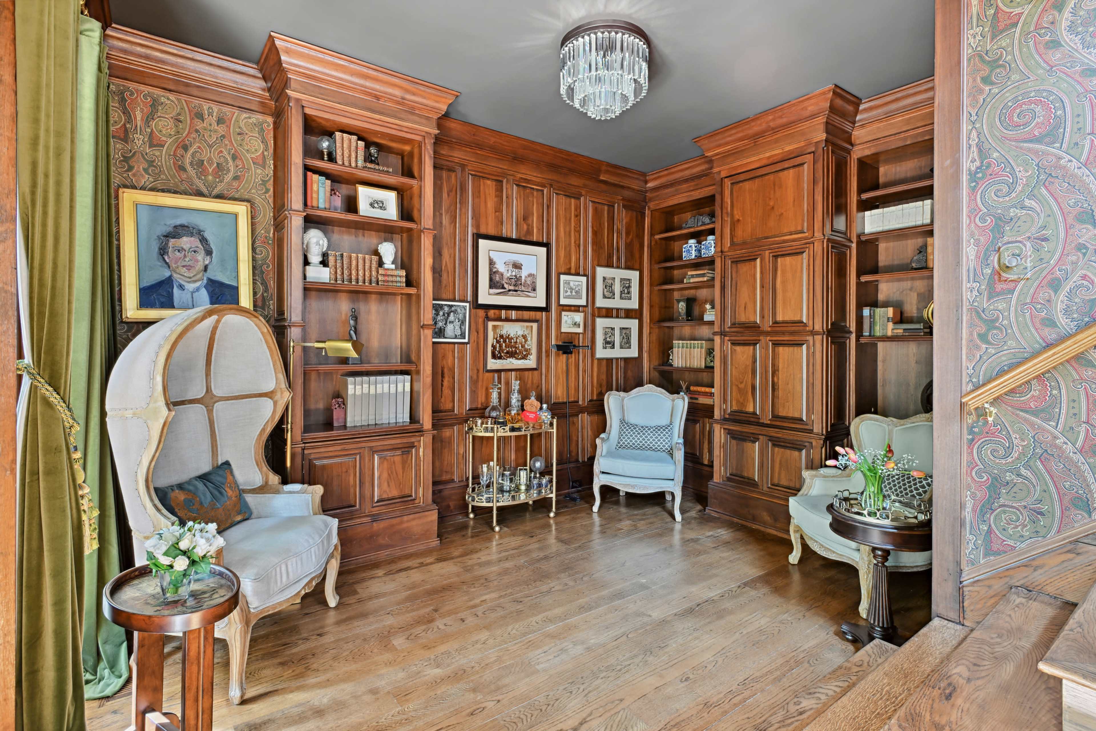 A wooden library with built-in bookshelves, two light-colored chairs, and a decorative display table.