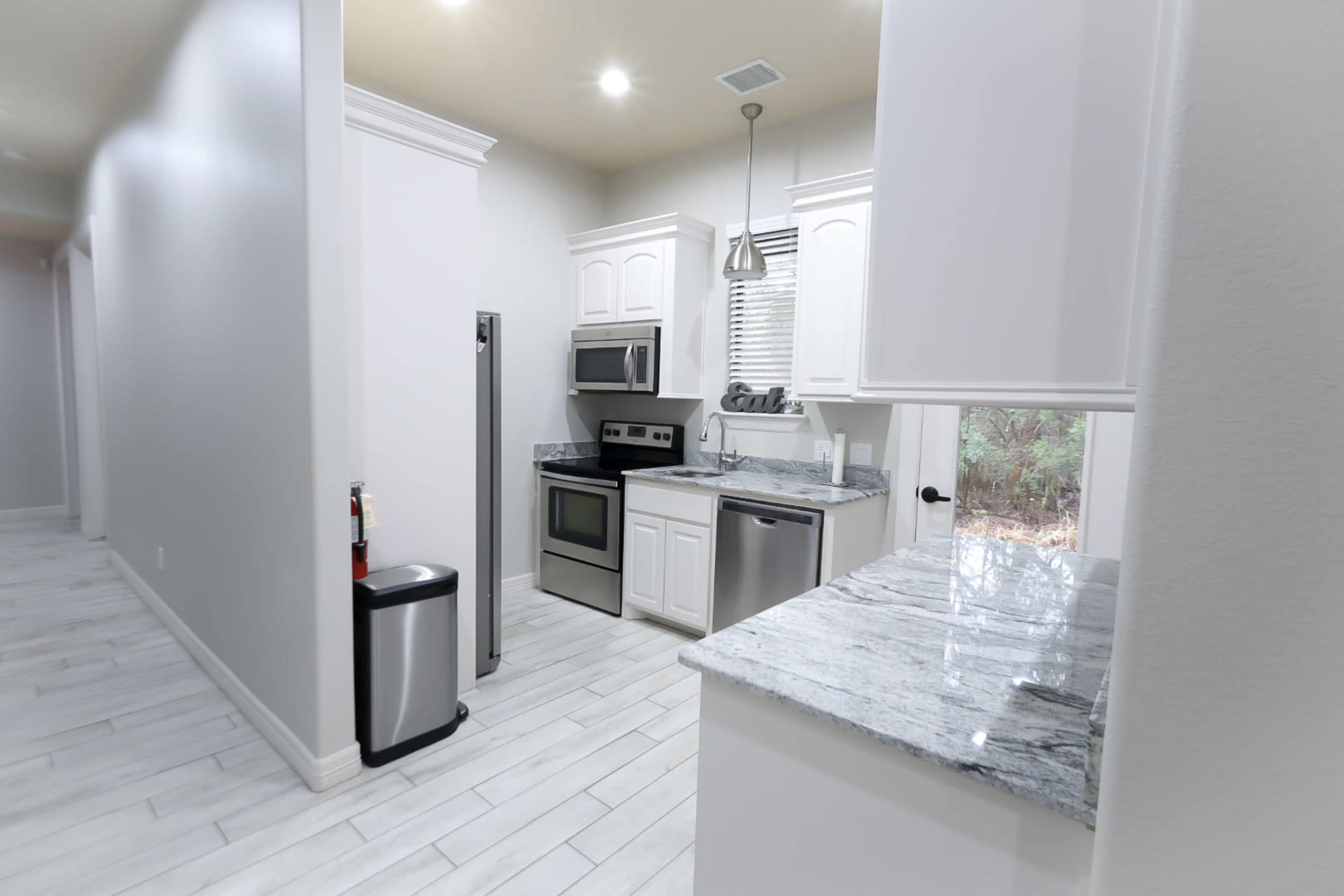 A modern kitchen featuring white cabinetry, stainless steel appliances, and a marble countertop.