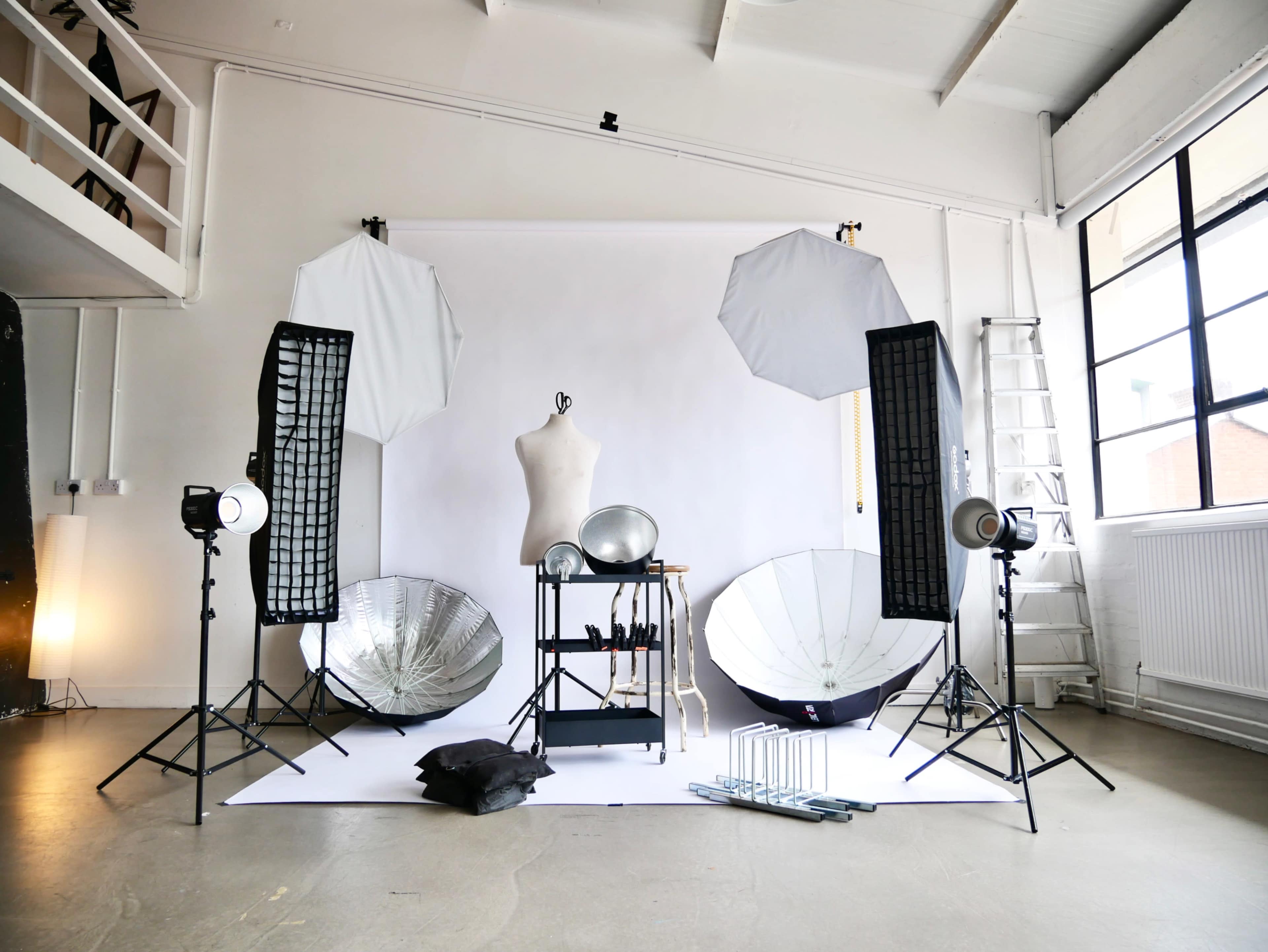 The image shows a photography studio set up with lighting equipment, reflectors, and a mannequin against a white backdrop.