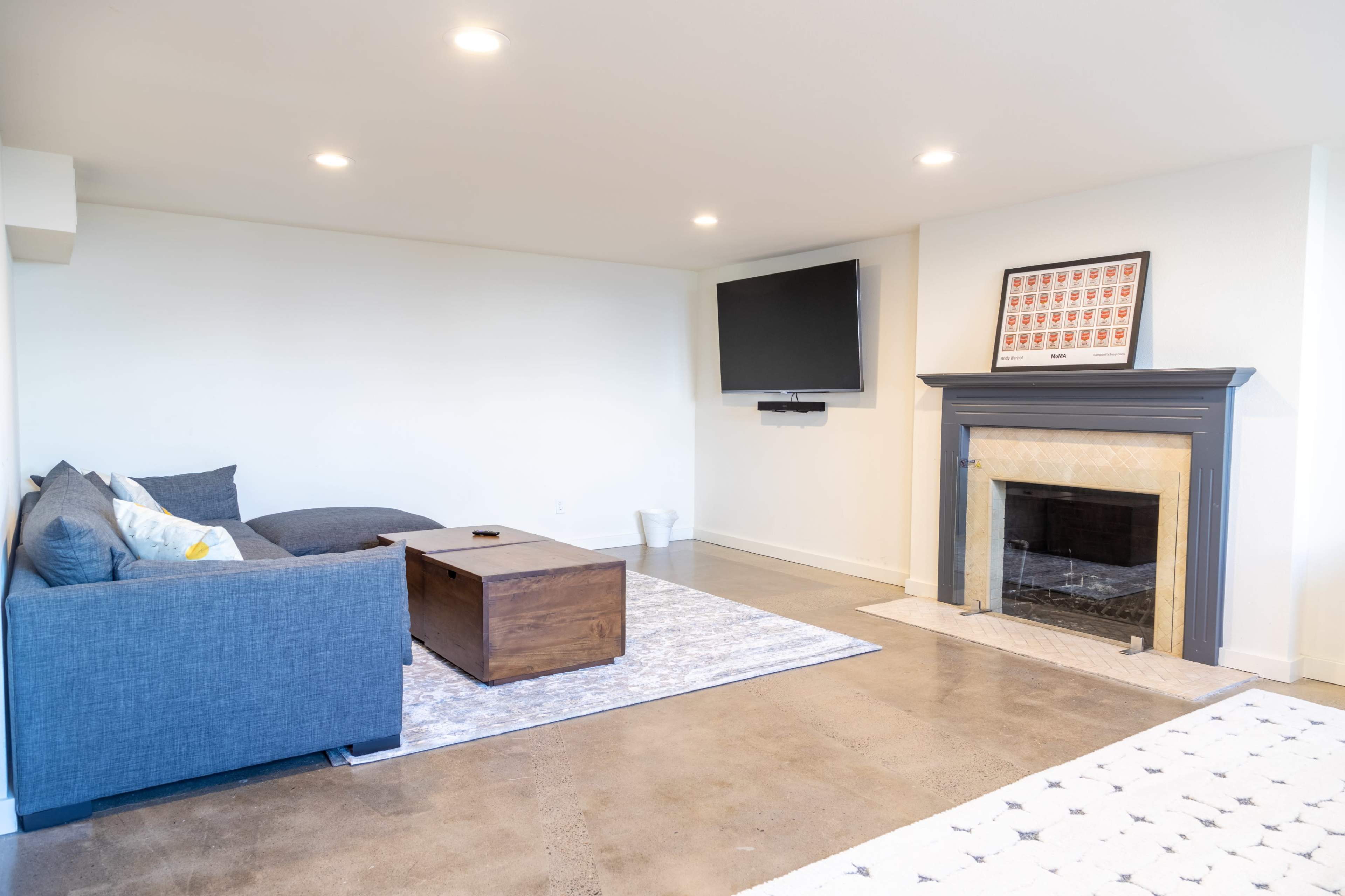 A modern living room features a gray sectional sofa, a wooden coffee table, and a fireplace with a mounted television above it.