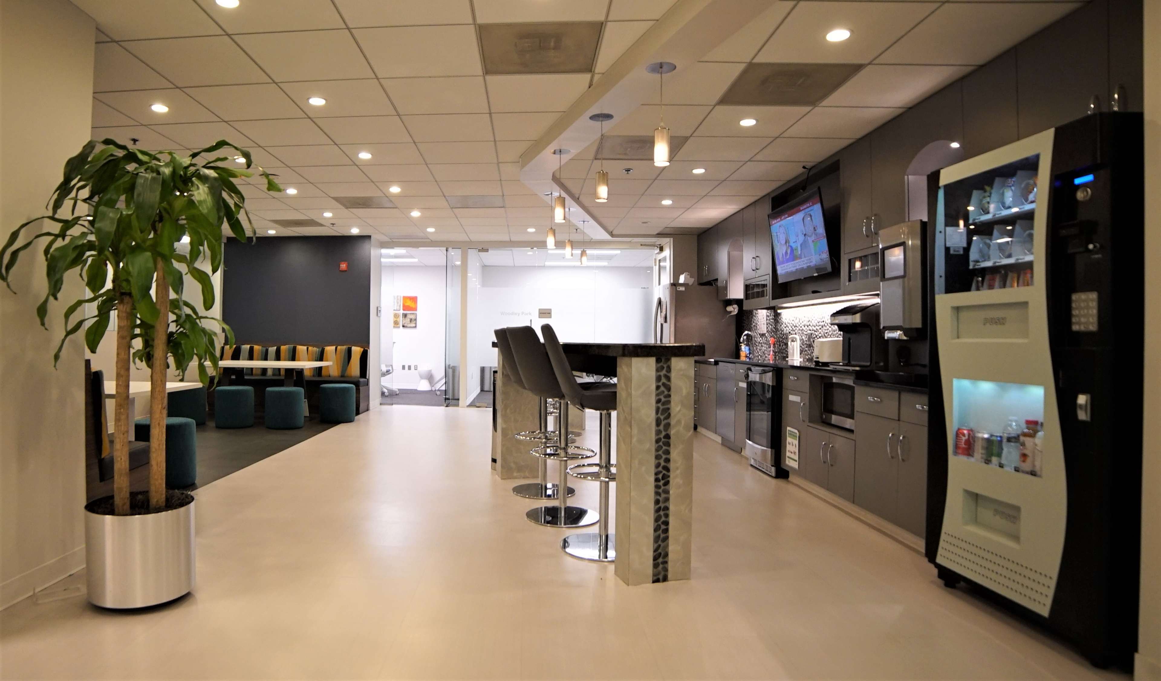A modern kitchen area with a bar counter, stools, and various appliances, including a vending machine and a television.