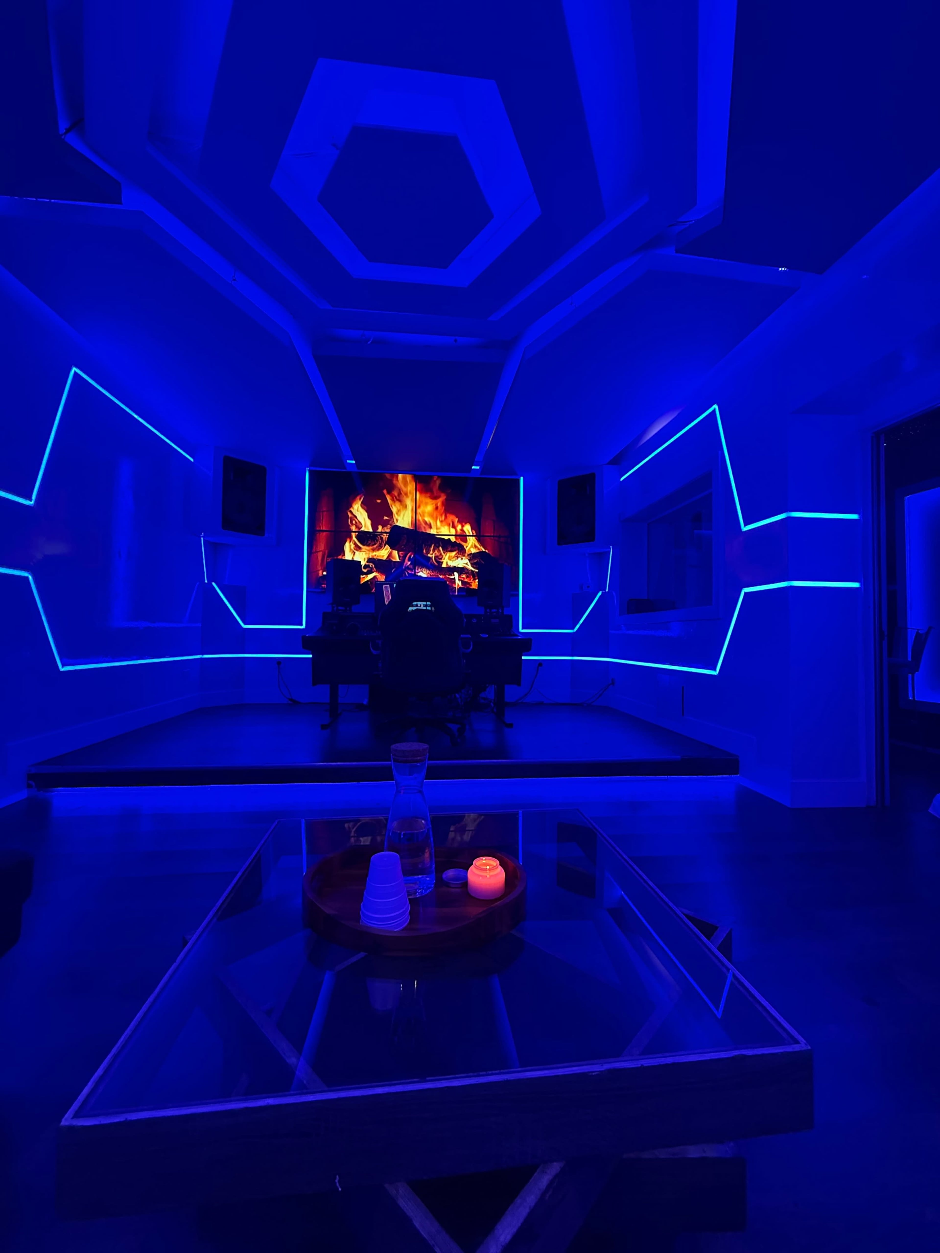 A modern room features a high-tech setup with a large screen displaying a fireplace, illuminated by blue LED lights.
