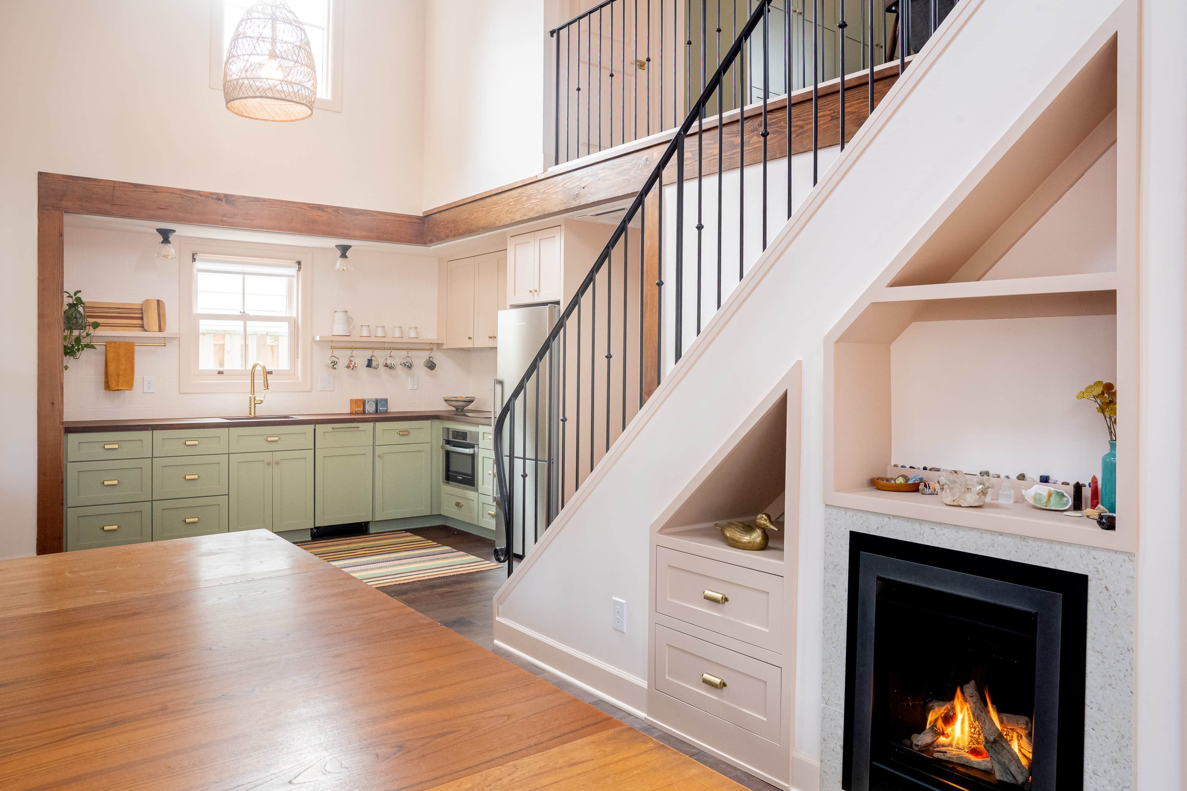 A modern kitchen with green cabinets and a staircase leading to an upper level, alongside a fireplace built into the wall.