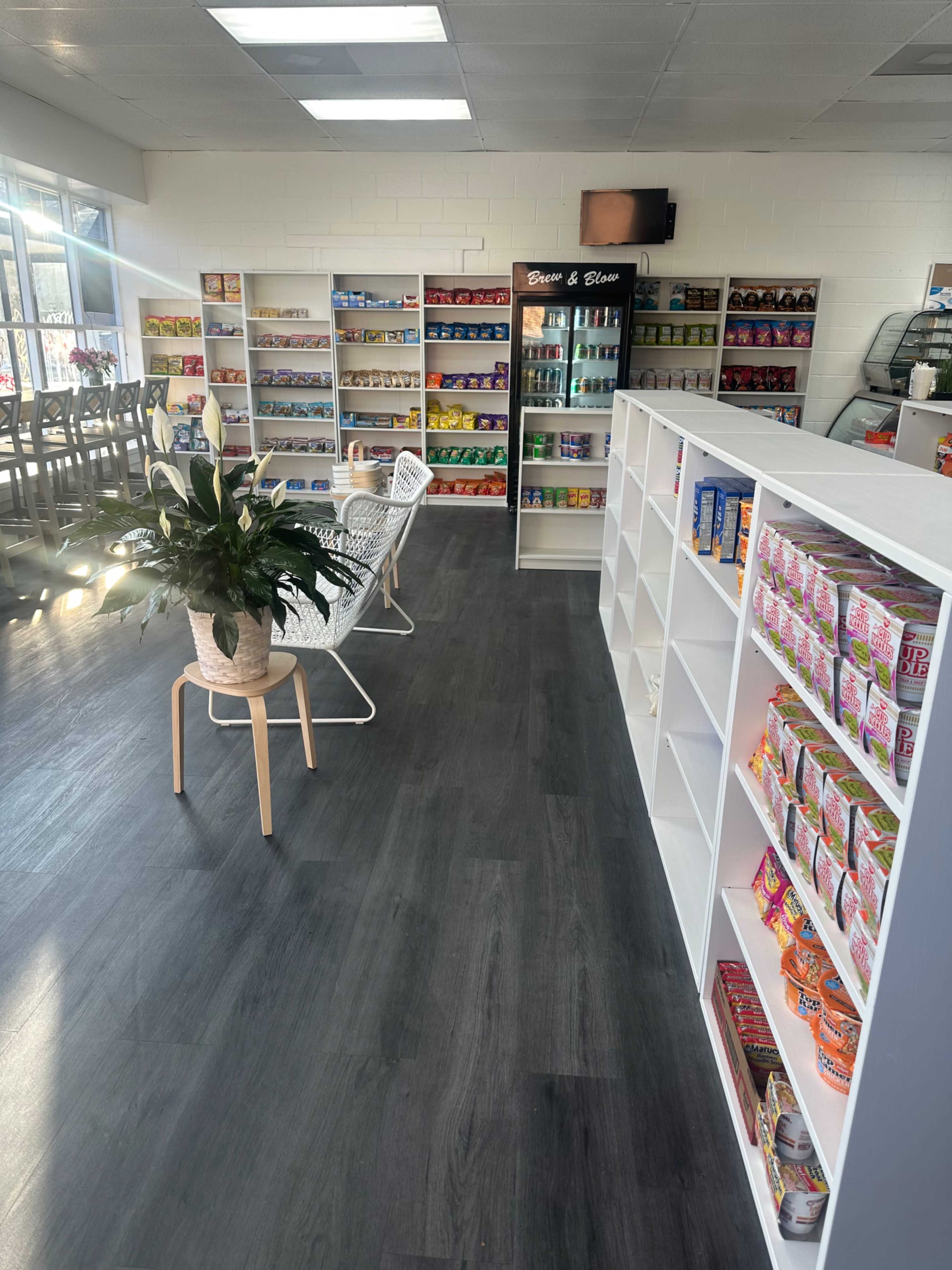 The image shows a brightly lit store interior featuring shelves stocked with various packaged items and a seating area with chairs and a table.